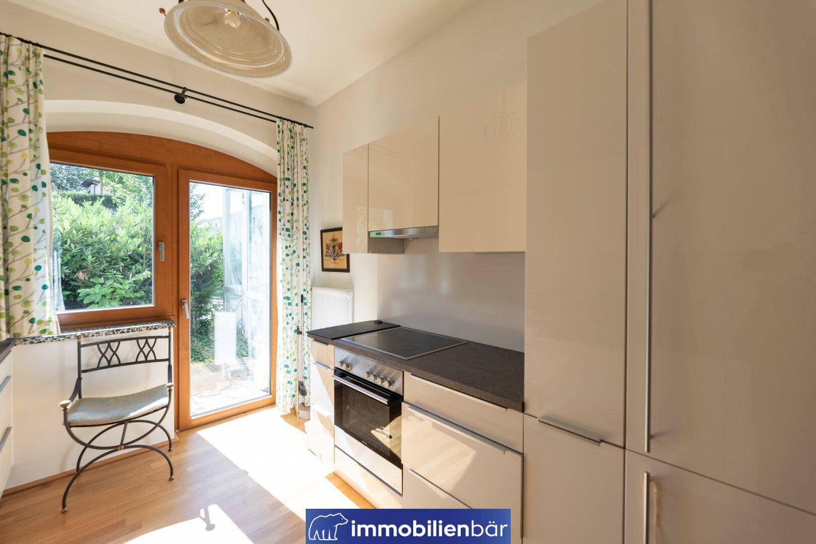 Helle, moderne Küche mit glänzenden Schränken, integriertem Backofen und Zugang zum Außenbereich.