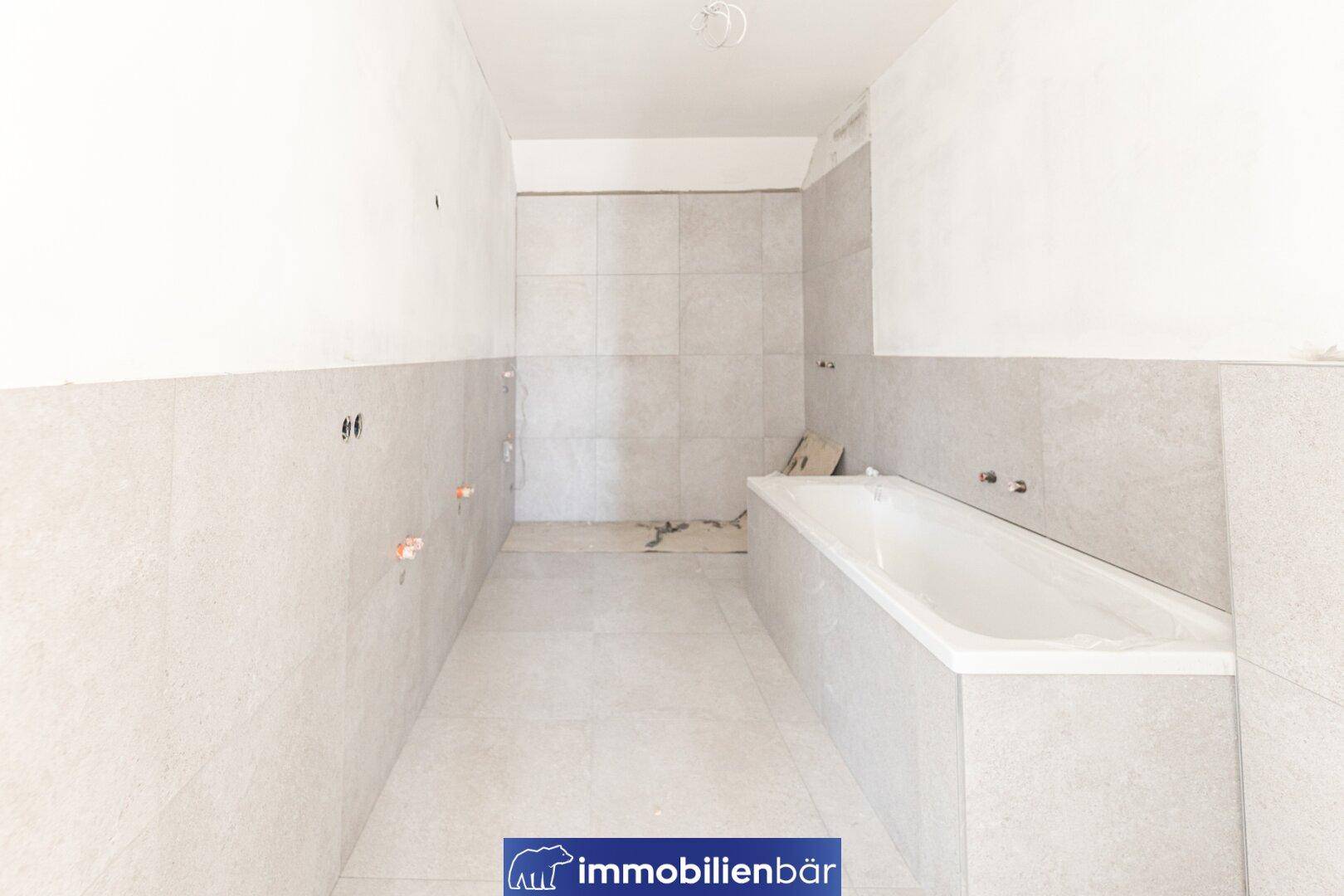 Unfertiges Badezimmer mit hellen Fliesen und eingebauter Badewanne, bereit für die Fertigstellung.