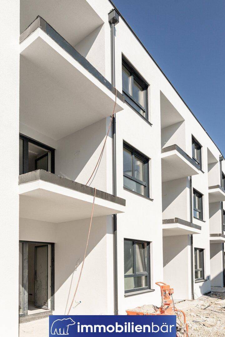 Moderne weiße Fassade eines Neubaus mit Balkonen unter klarem blauem Himmel.