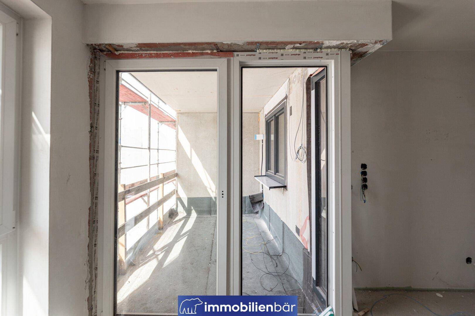 Detailansicht einer großen Fenstertür, die zu einem im Bau befindlichen Außenbereich führt.