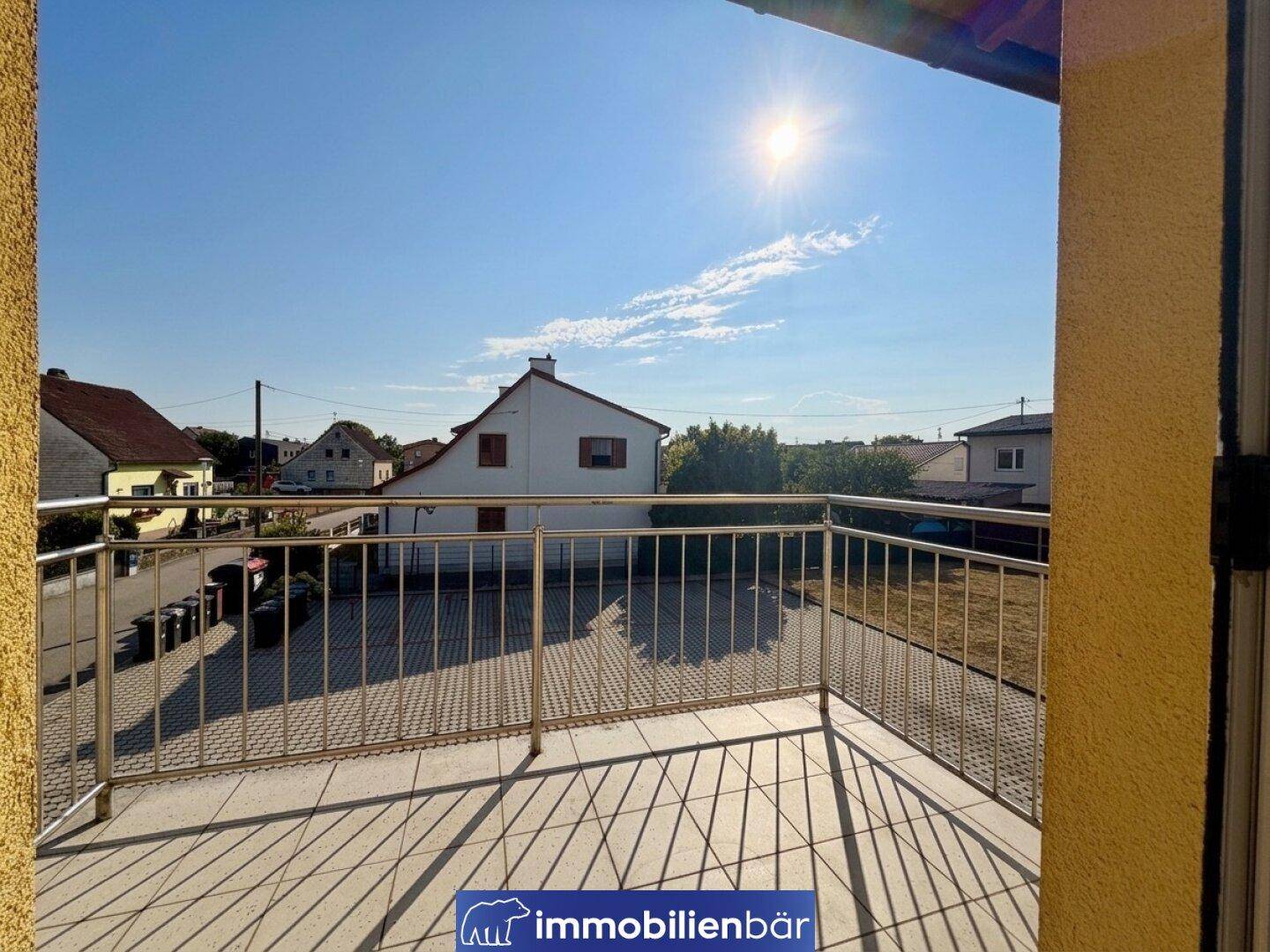 Sonniger Balkon mit Metallgeländer und Blick auf die umliegenden Häuser und die Nachbarschaft.