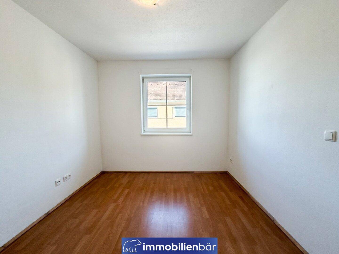 Leeres Schlafzimmer mit Holzboden und einem Fenster, das Tageslicht hereinlässt, ideal zur individuellen Einrichtung.