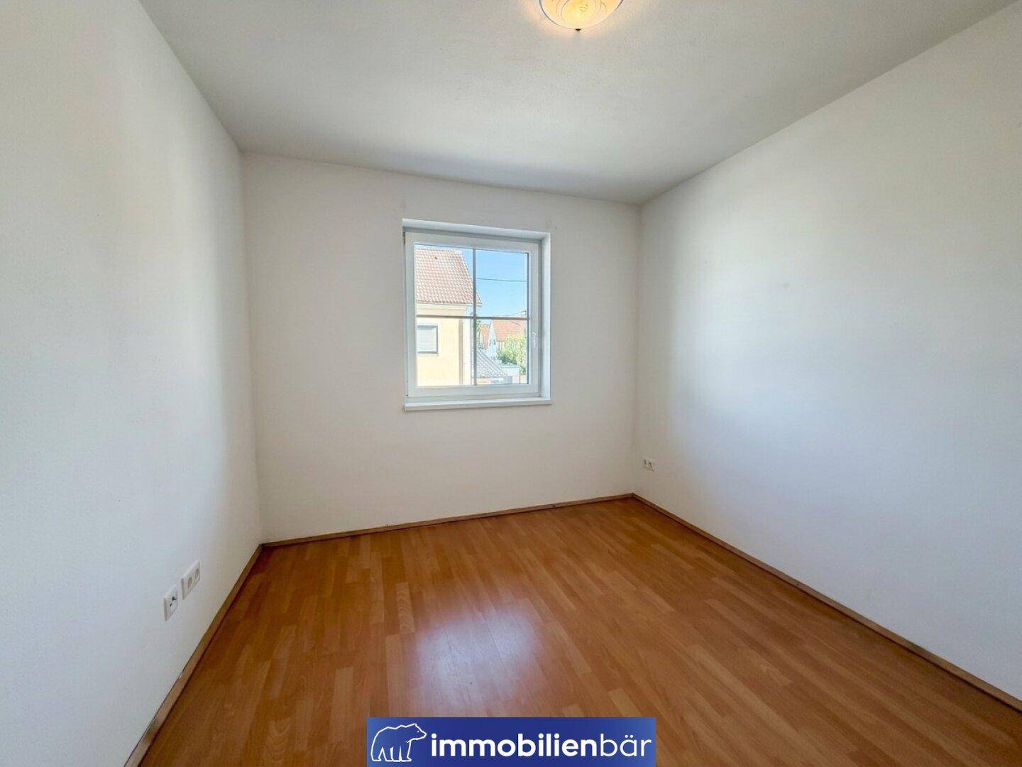 Ruhiges Schlafzimmer mit hellem Holzboden und einem Fenster, das einen Blick auf die Umgebung bietet.