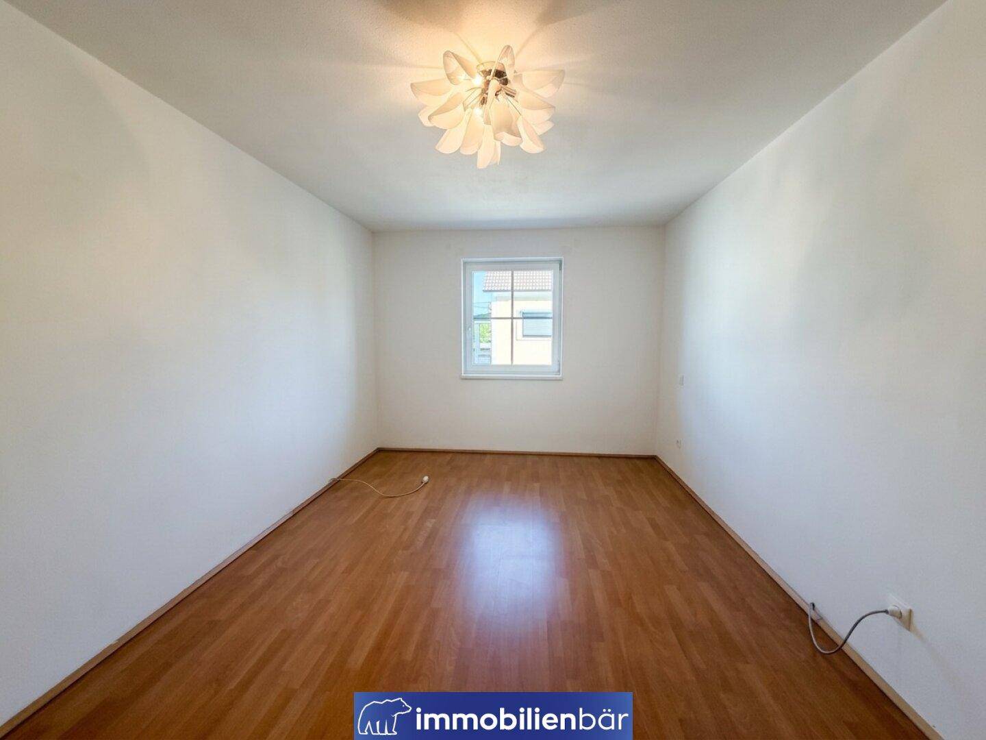 Geräumiges Schlafzimmer mit Holzboden und einer modernen Deckenleuchte, bereit für neue Bewohner.