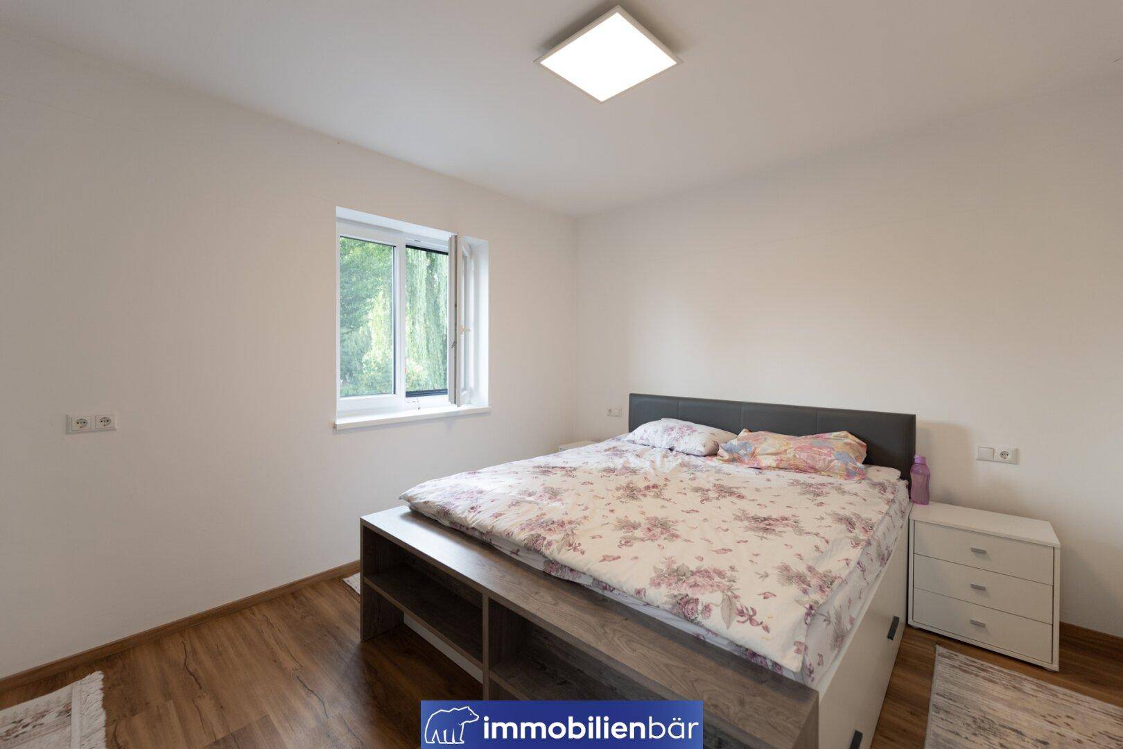 Helles Schlafzimmer mit Doppelbett, Laminatboden und Fenster mit Blick ins Grüne.