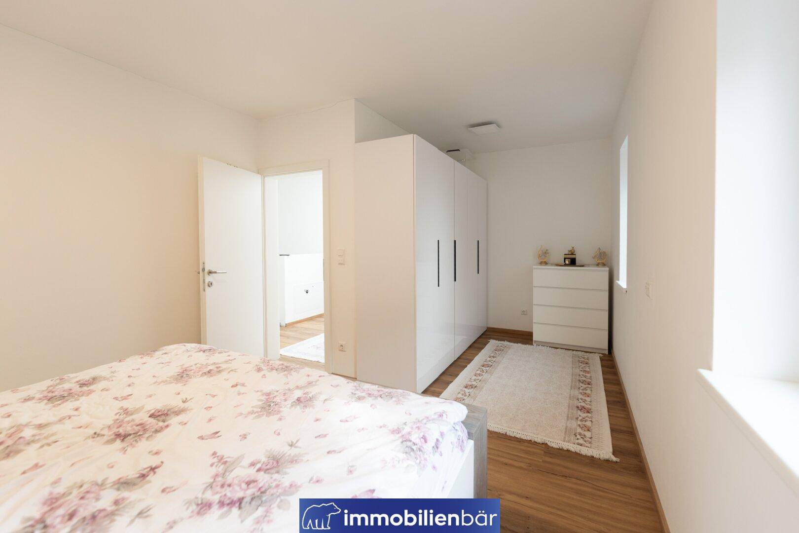 Schlafzimmer mit Doppelbett, weißem Kleiderschrank und Laminatboden.