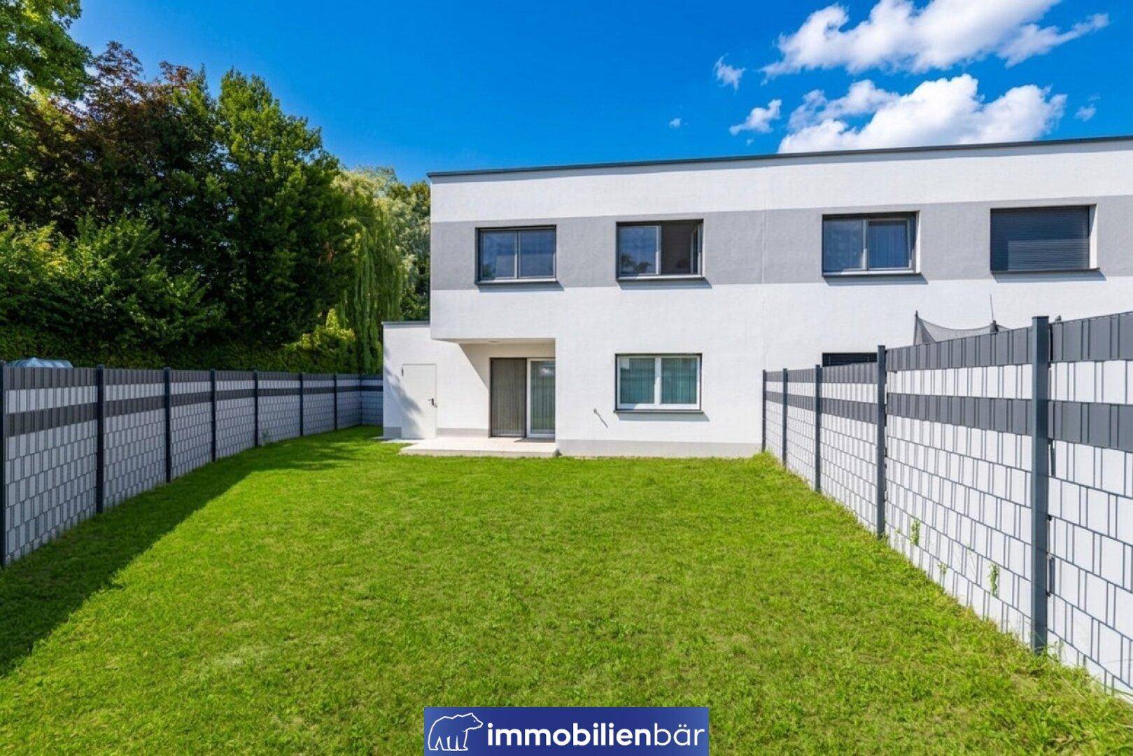 Rückansicht der modernen Doppelhaushälfte mit umzäuntem Garten und Rasenfläche.