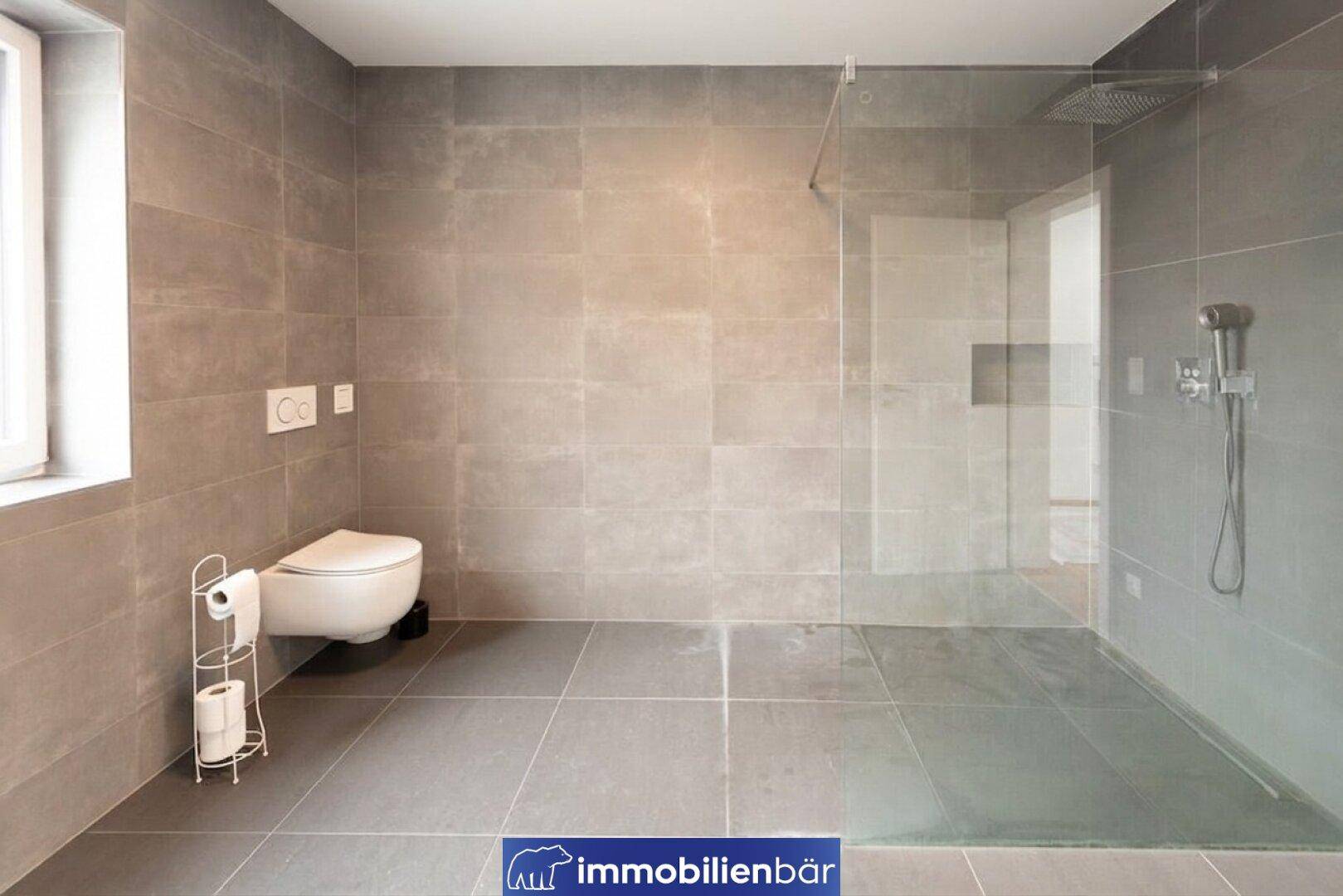 Modernes Badezimmer mit großer ebenerdiger Dusche, WC und grauen Fliesen.