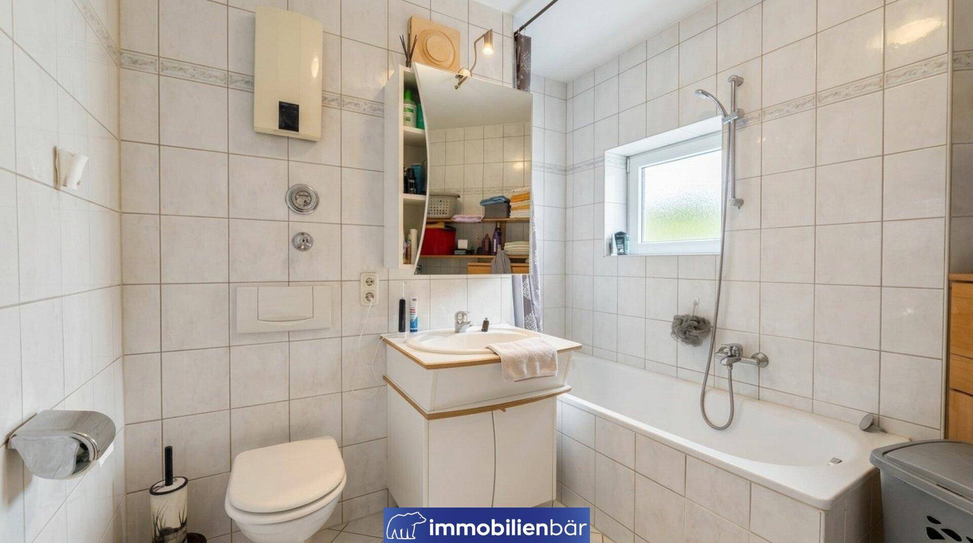 Gefliestes Badezimmer mit Badewanne, Toilette, Waschbecken und Fenster für Tageslicht.