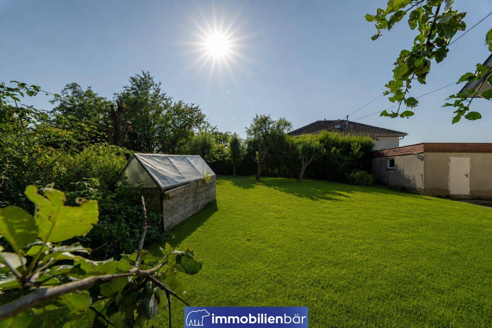 Großer, gepflegter Garten mit Rasenfläche, Bäumen und einem kleinen Gewächshaus.