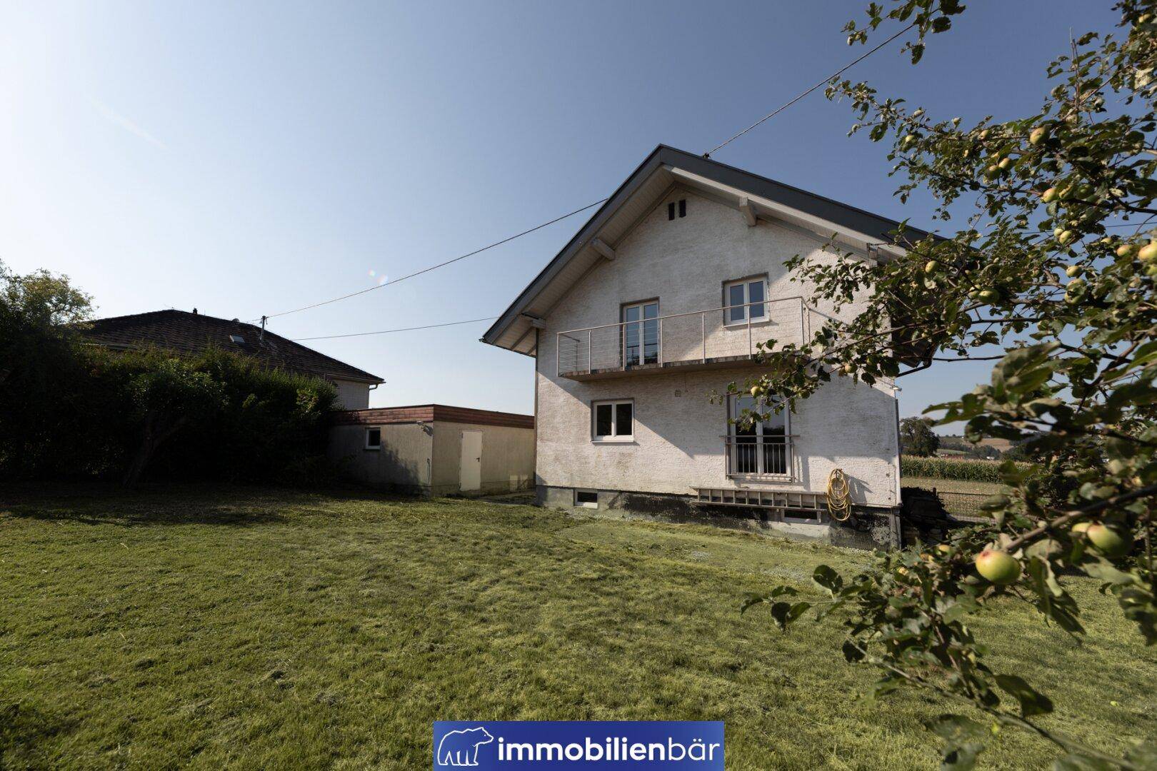 Weißes Einfamilienhaus mit Satteldach, Balkon und großem grünen Garten.