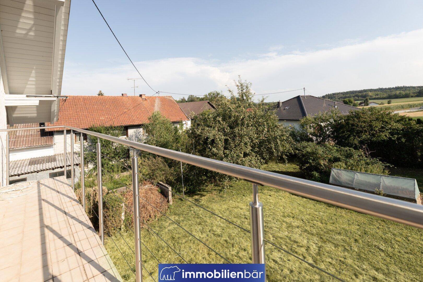 Balkon mit Edelstahlgeländer und weitem Blick über die umliegende Landschaft und Dächer.