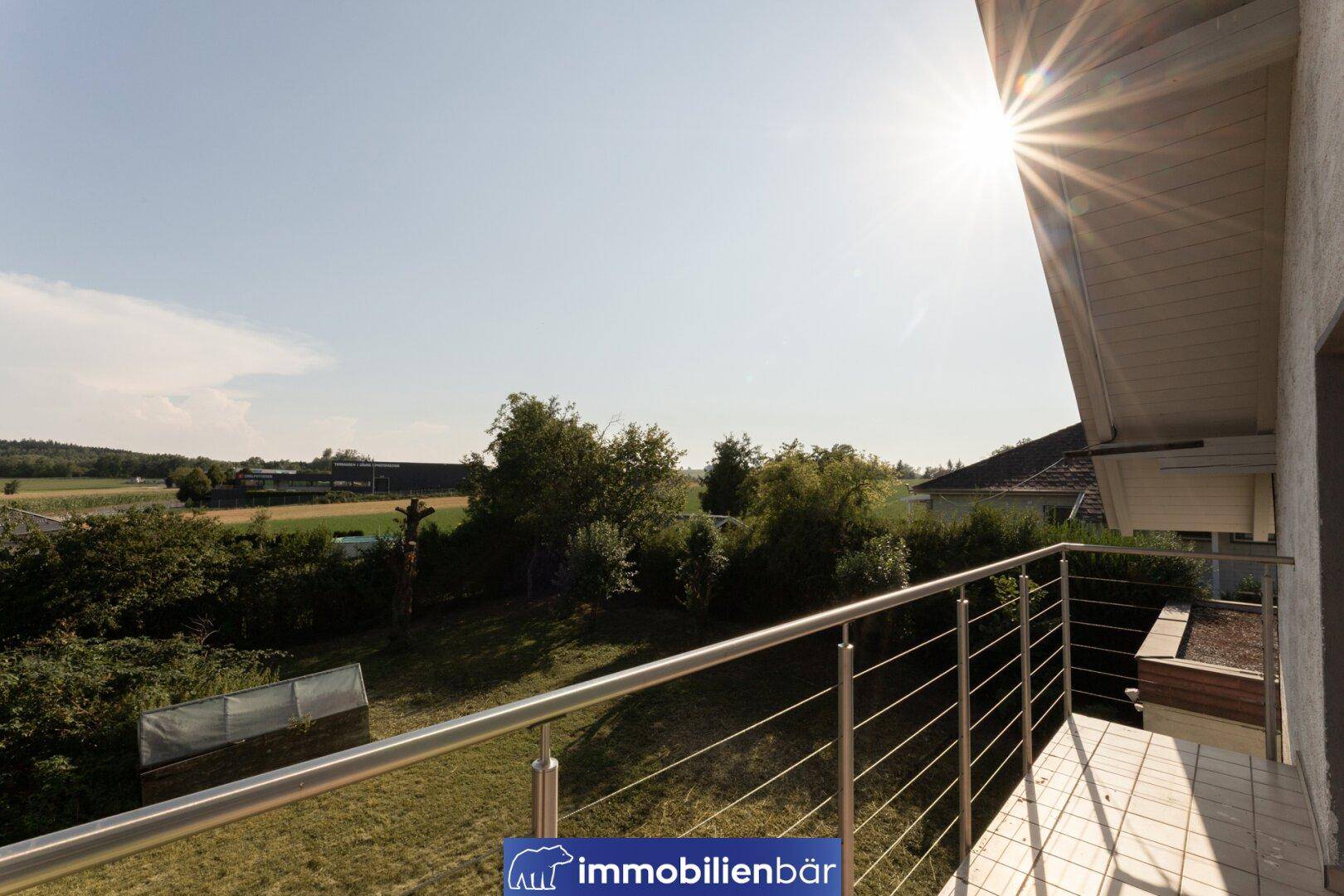 Balkon mit Edelstahlgeländer und weitem Blick über den grünen Garten und die Landschaft.