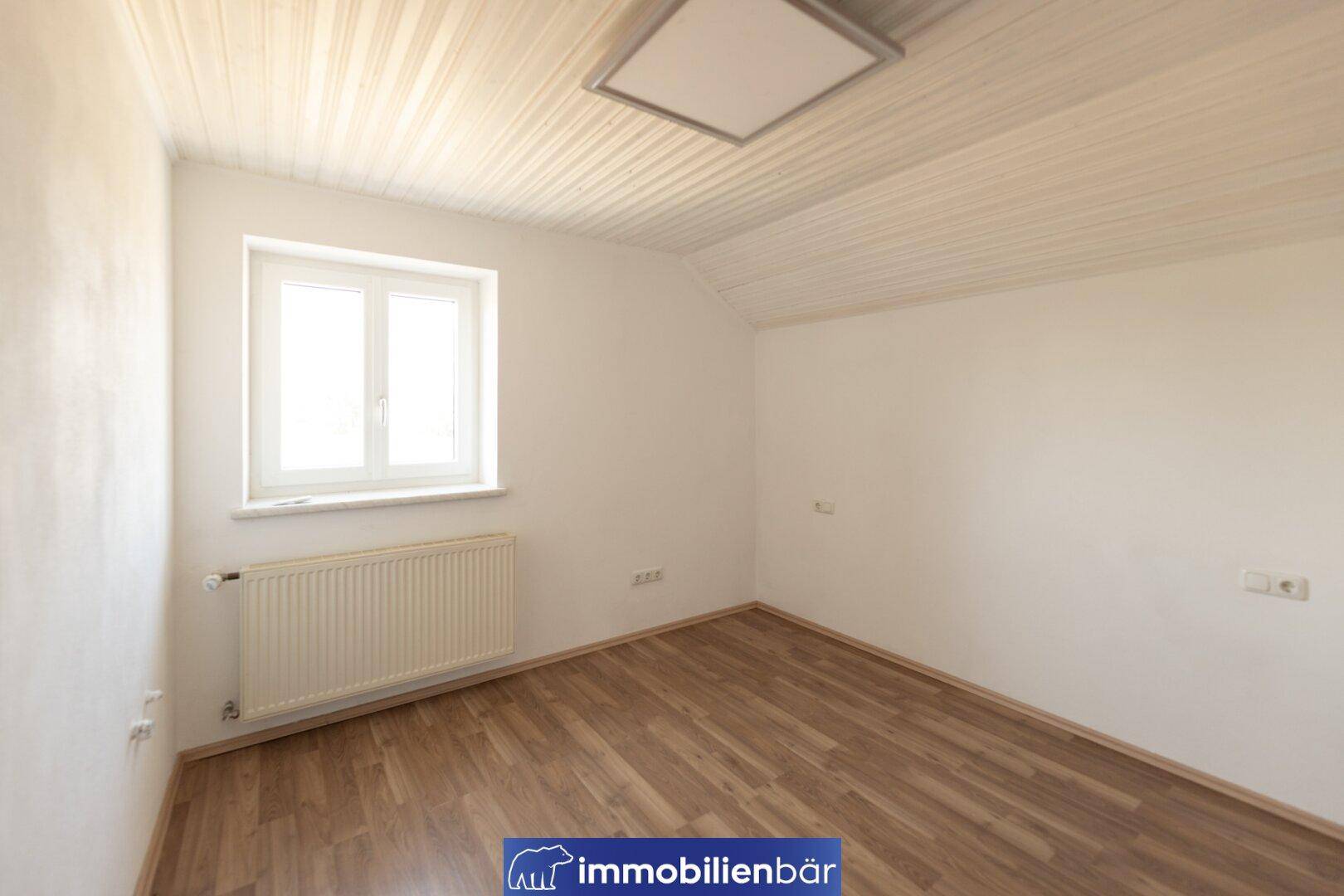 Gemütliches Schlafzimmer mit Dachschräge, Laminatboden und einem Fenster.