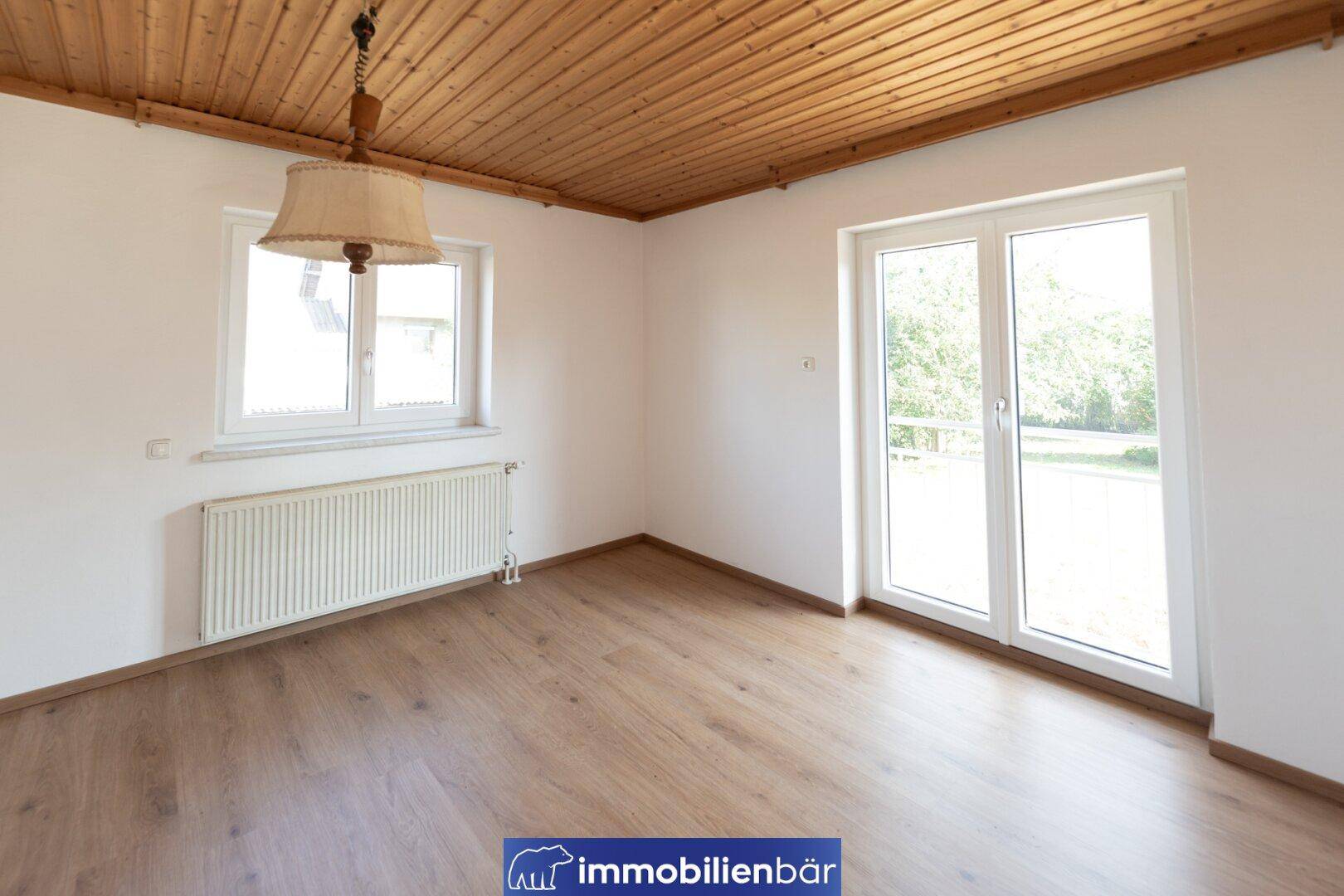 Helles Zimmer mit Holzbalkendecke, Laminatboden und Zugang zu einem Balkon.