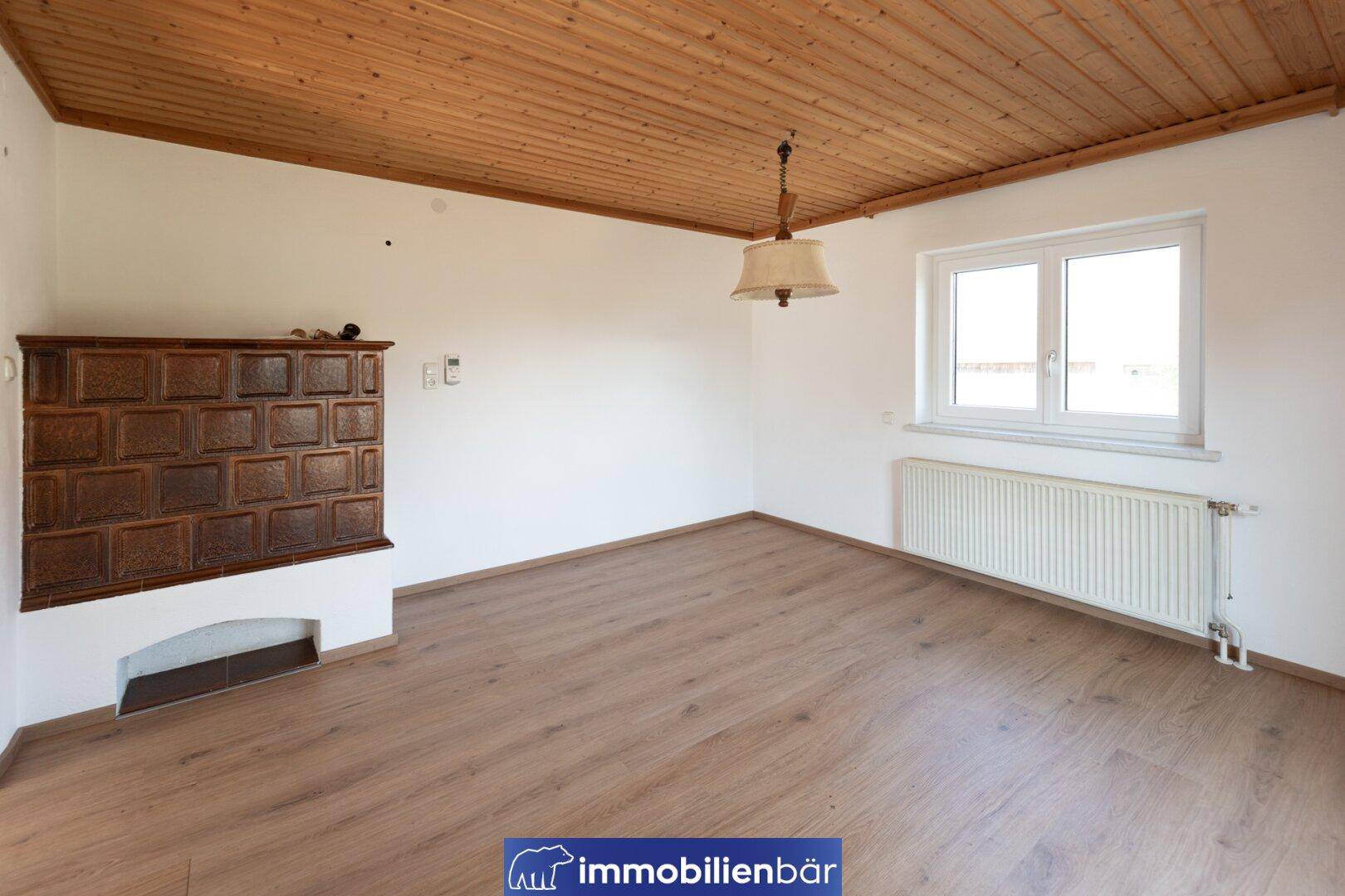 Helles Zimmer mit Holzbalkendecke, Laminatboden und traditionellem Kachelofen.