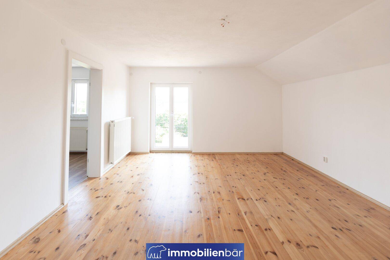 Geräumiges Zimmer mit Holzdielenboden und Zugang zu einem Balkon, hell und freundlich.
