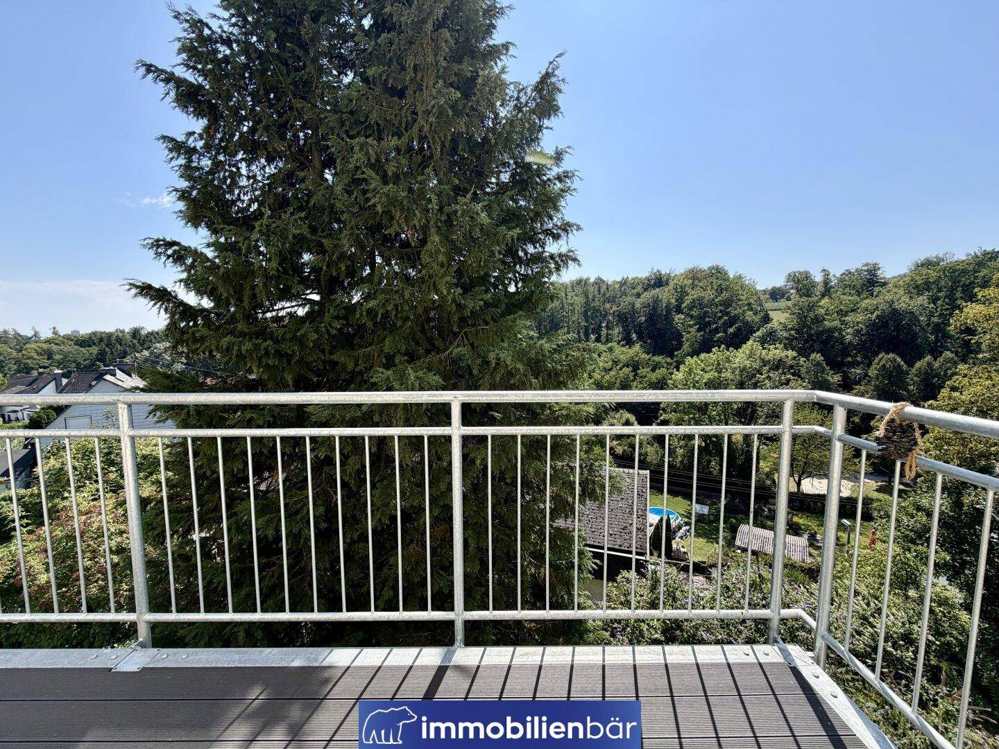Heller Balkon mit Metallgeländer und schöner Aussicht auf die bewaldete Umgebung.