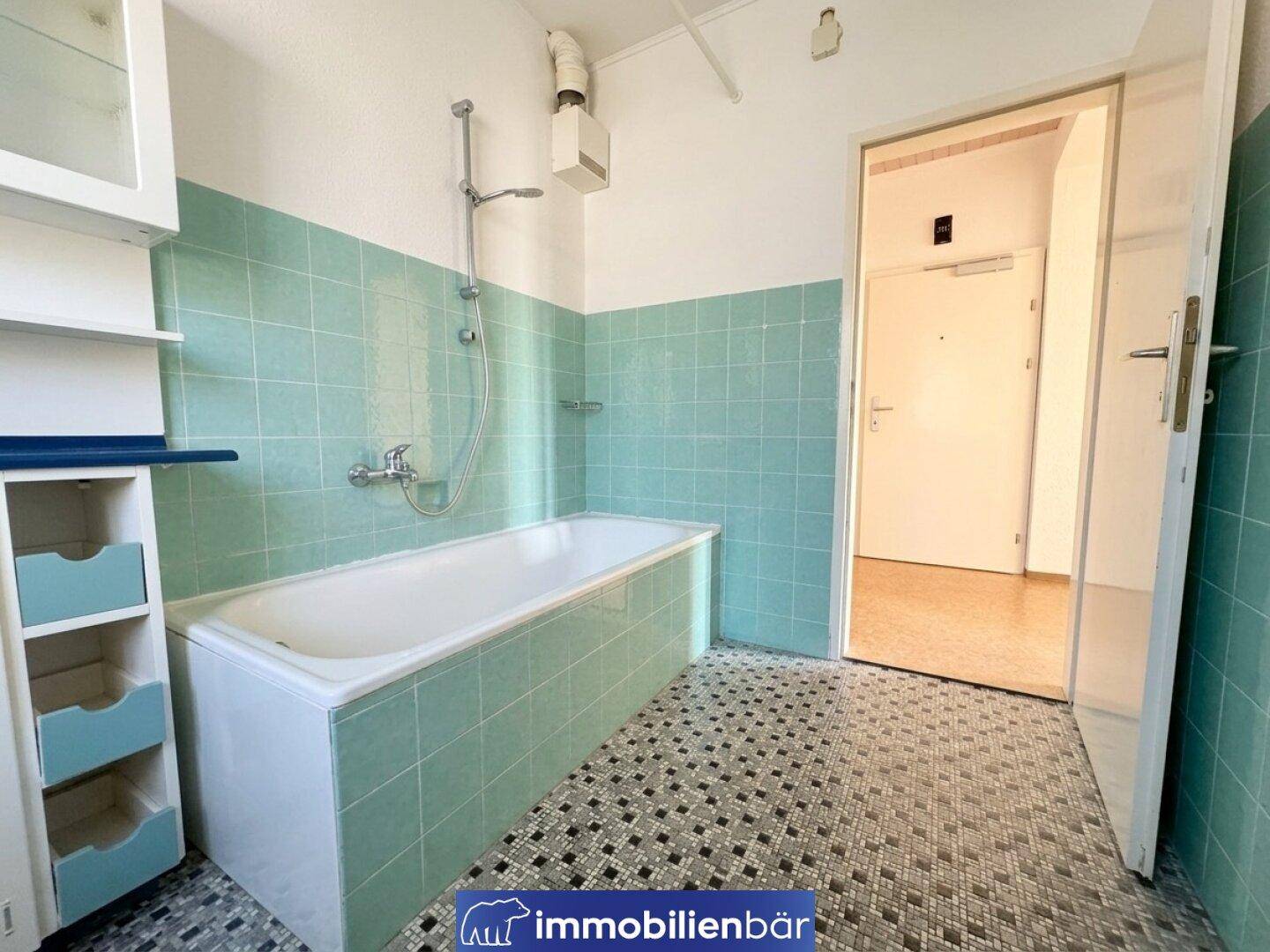 Retro-Badezimmer mit Badewanne, Duschvorrichtung und charakteristischen grünen Wandfliesen.