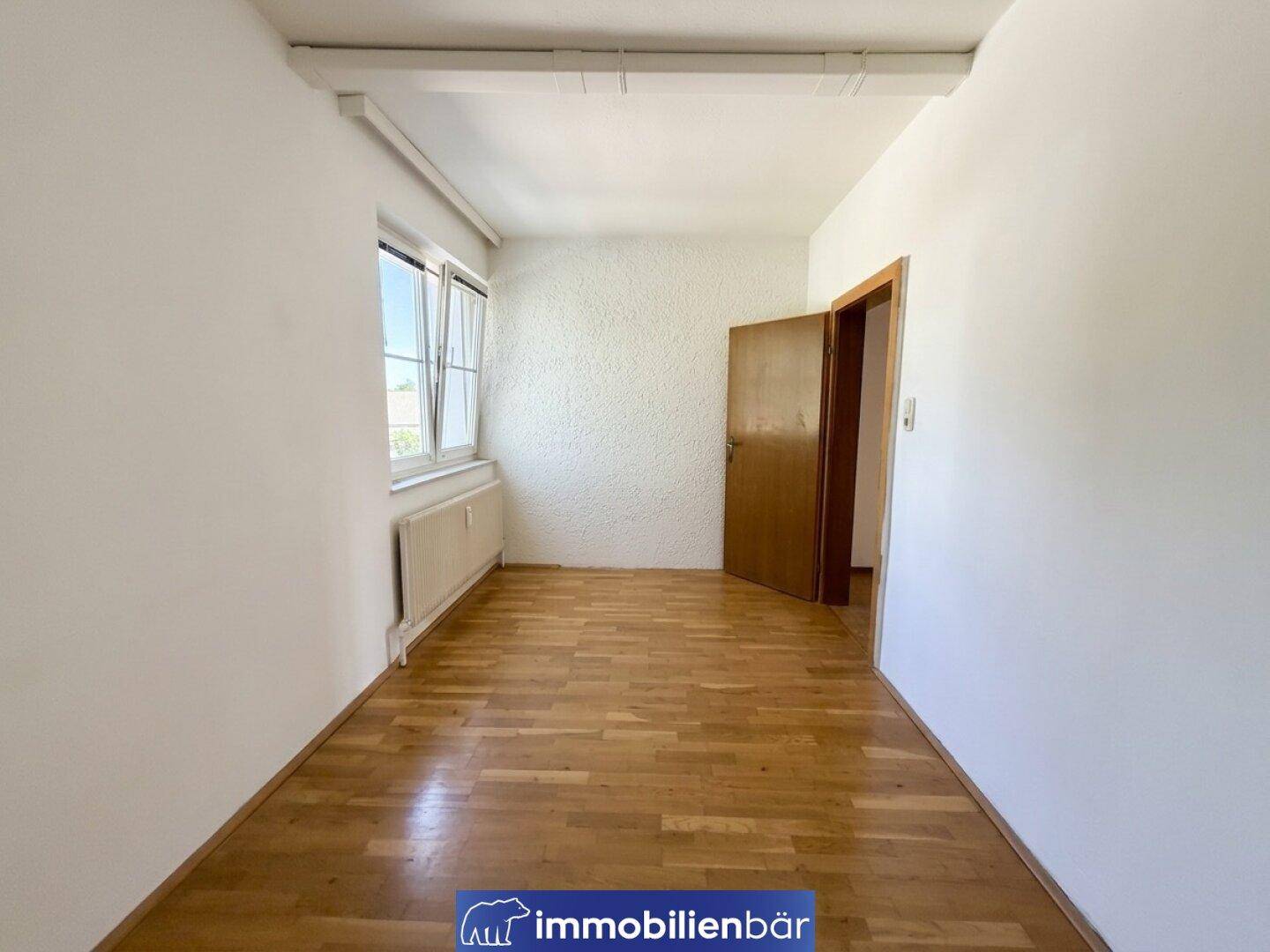Helles, unmöbliertes Zimmer mit Holzparkettboden und einem Fenster für natürliche Belichtung.