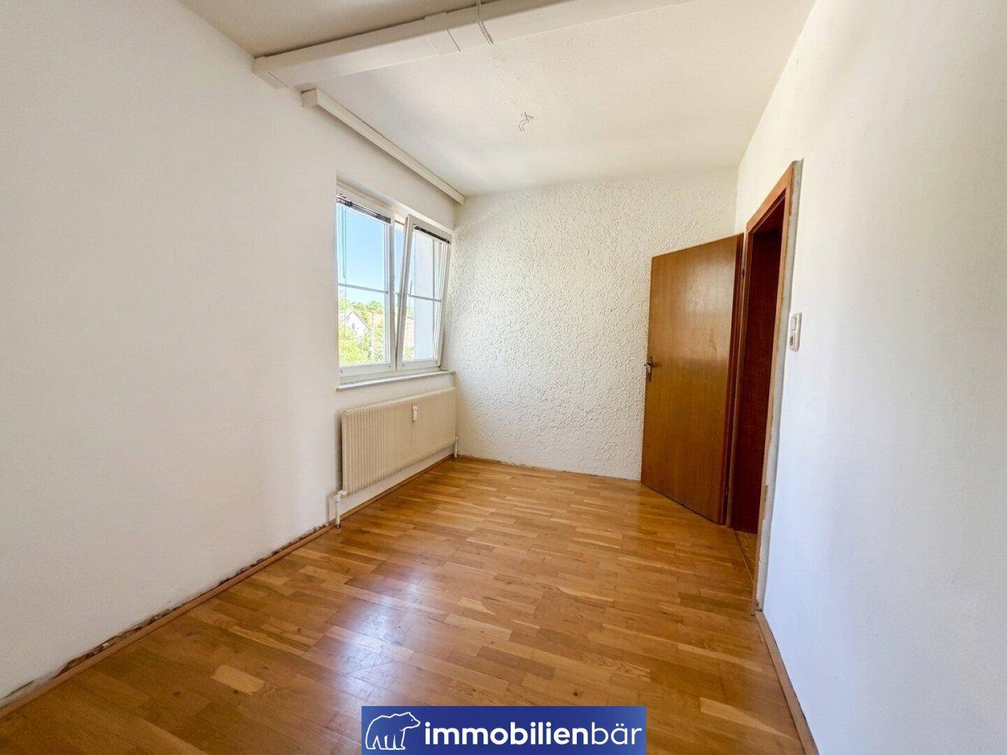 Leeres Zimmer mit schönem Parkettboden und einem Fenster, das den Raum erhellt.
