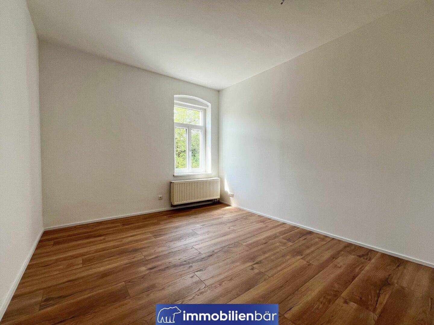 Helles Zimmer mit Laminatboden und einem Fenster, das viel Tageslicht hereinlässt.