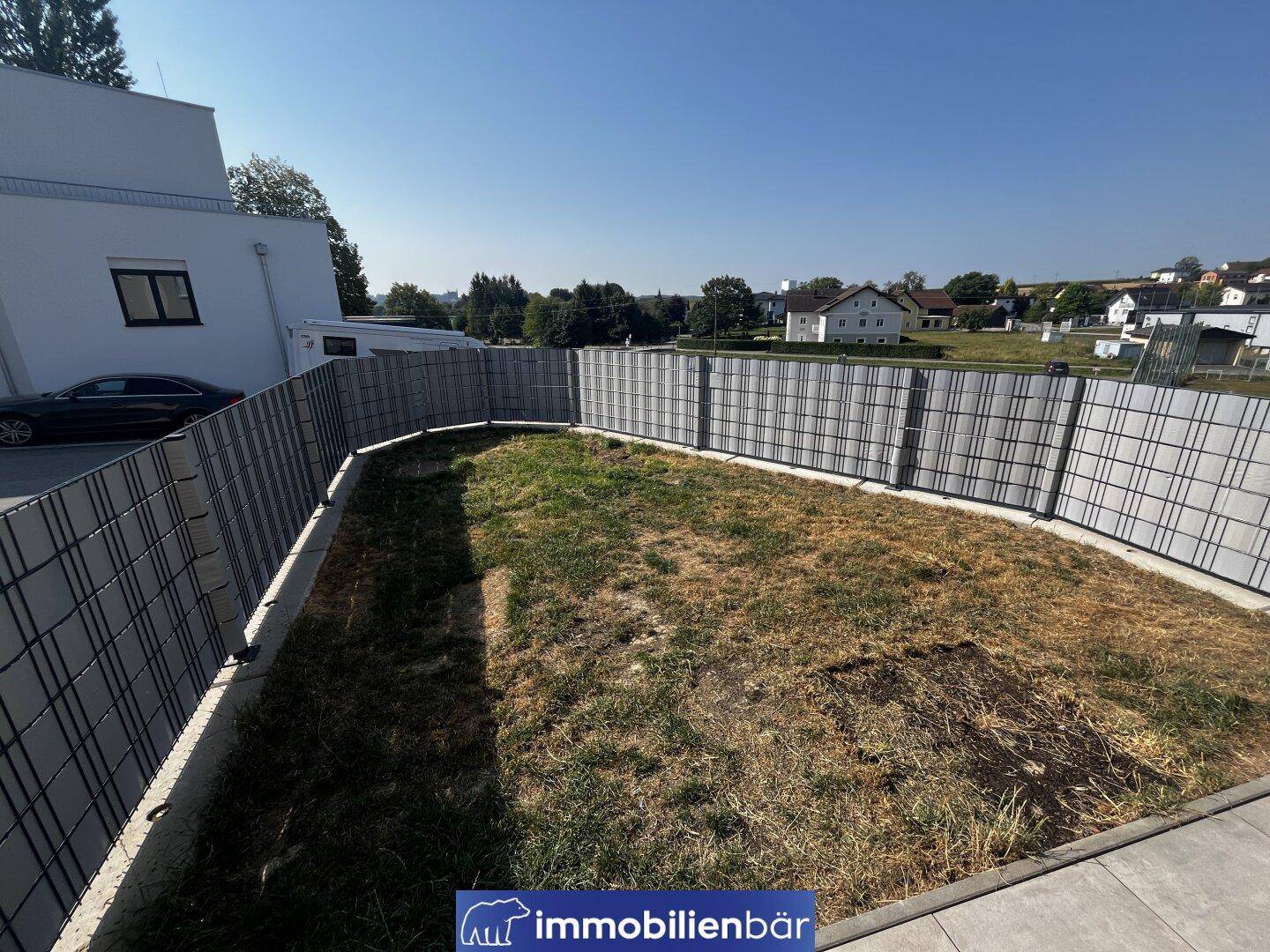 Gartenfläche mit Zaun und weitem Blick auf die grüne Umgebung und weitere Häuser in der Ferne.