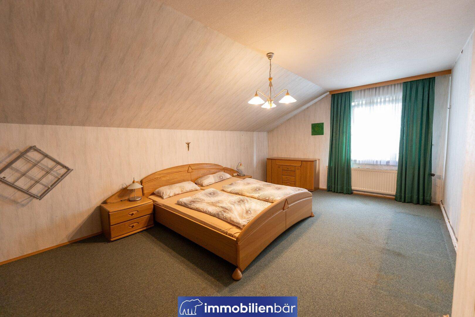 Schlafzimmer im Dachgeschoss mit Doppelbett, Teppichboden und schrägen Wänden, gemütlich und hell.