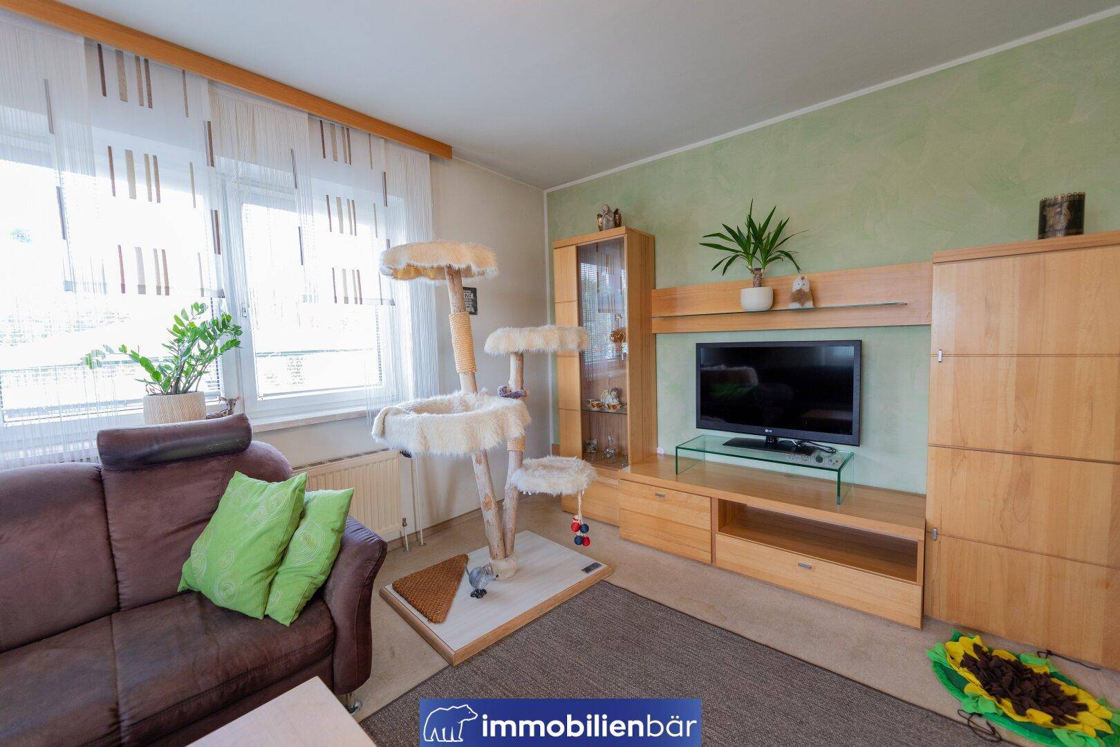Wohnzimmer mit TV-Möbeln aus Holz, großem Fenster und Katzenbaum, hell und einladend.