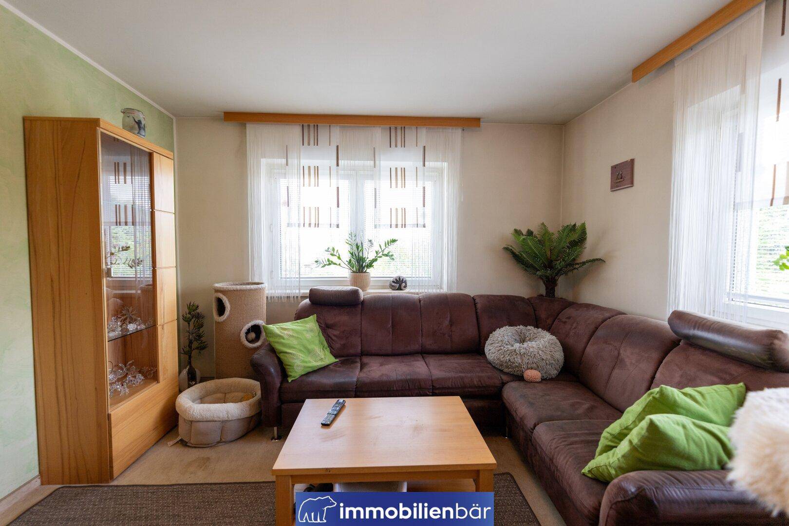 Gemütliches Wohnzimmer mit braunem Ecksofa, Holztisch und hellem Fenster, ideal zum Entspannen.