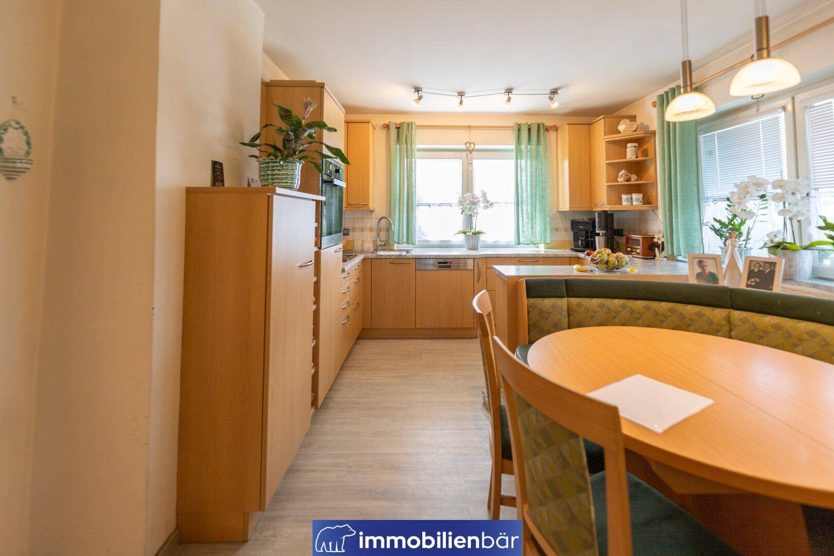 Geräumige Küche mit Essecke, Holzmöbeln und hellem Laminatboden, gut beleuchtet durch Fenster.