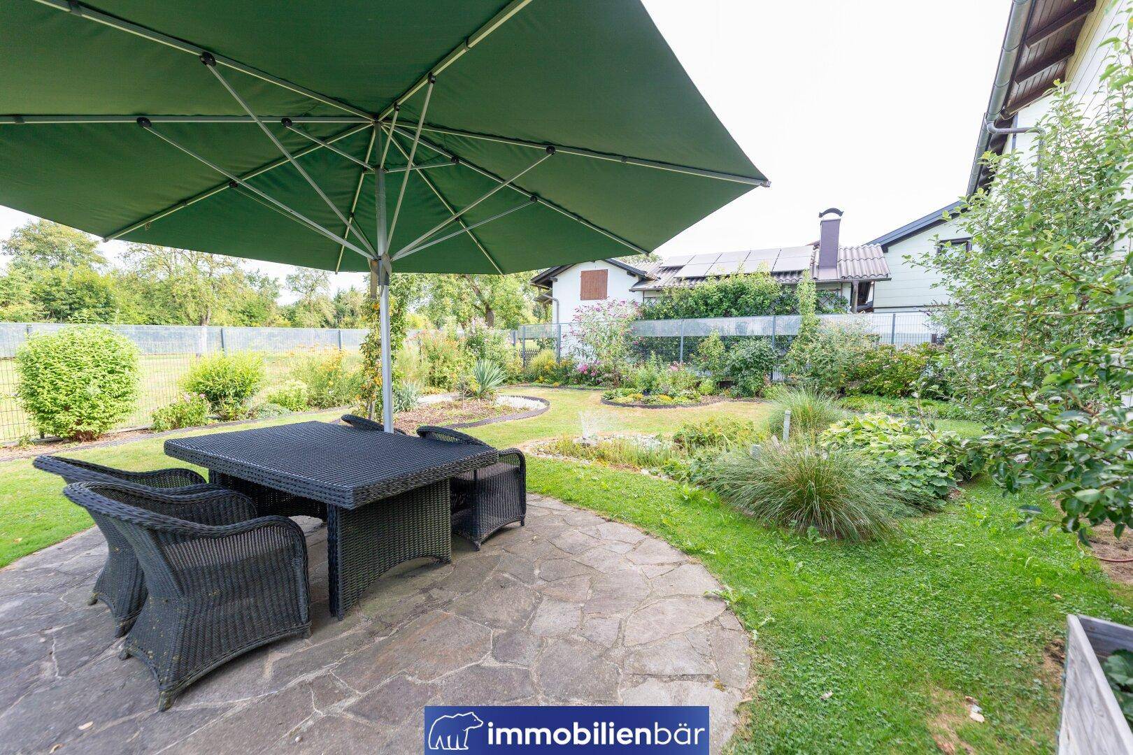 Gepflasterte Terrasse mit Rattanmöbeln und großem Sonnenschirm, umgeben von Garten.