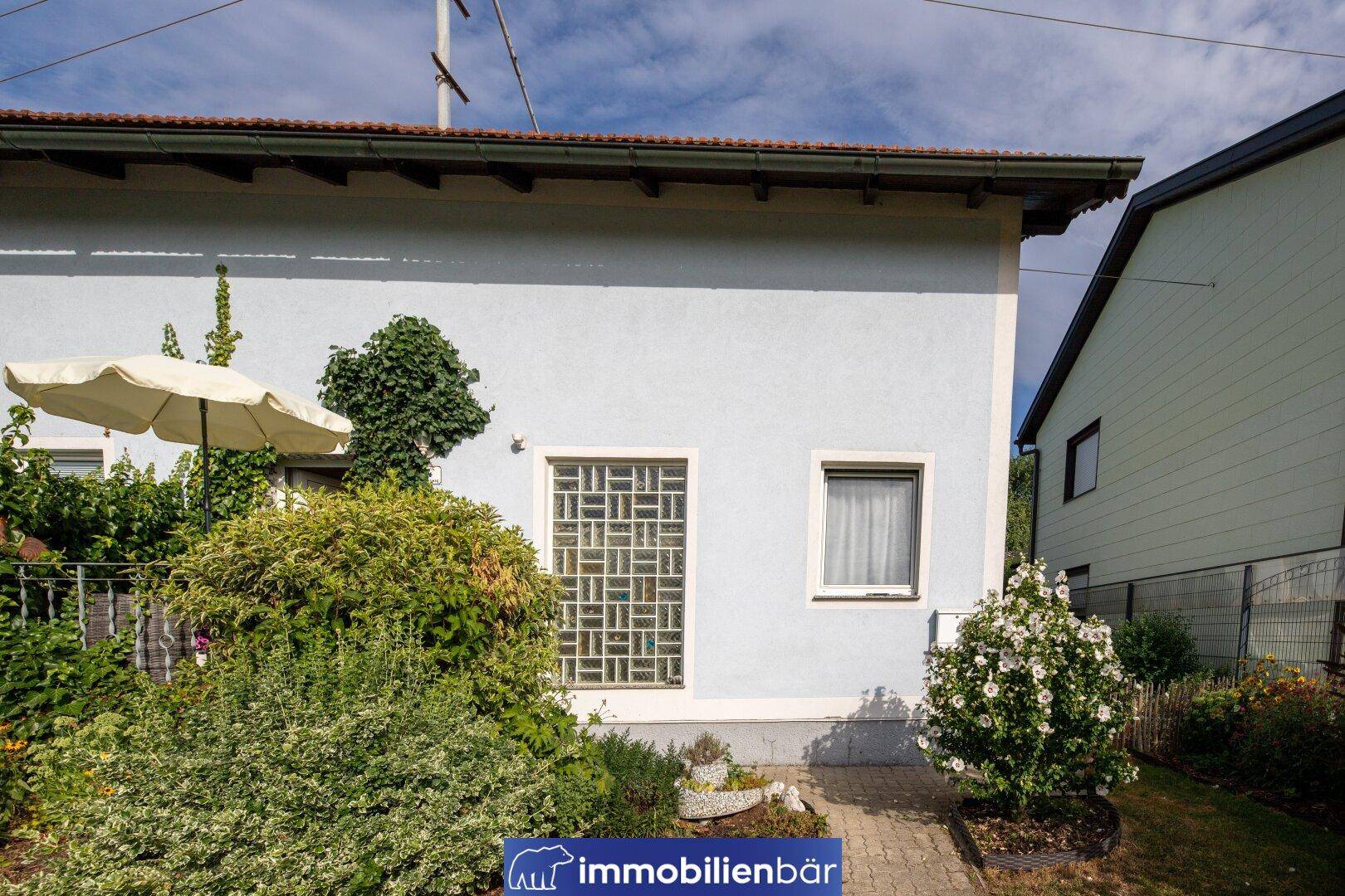 Nahaufnahme der Hausfassade mit einem Fenster und einem gepflegten Blumenbeet im Vordergrund.