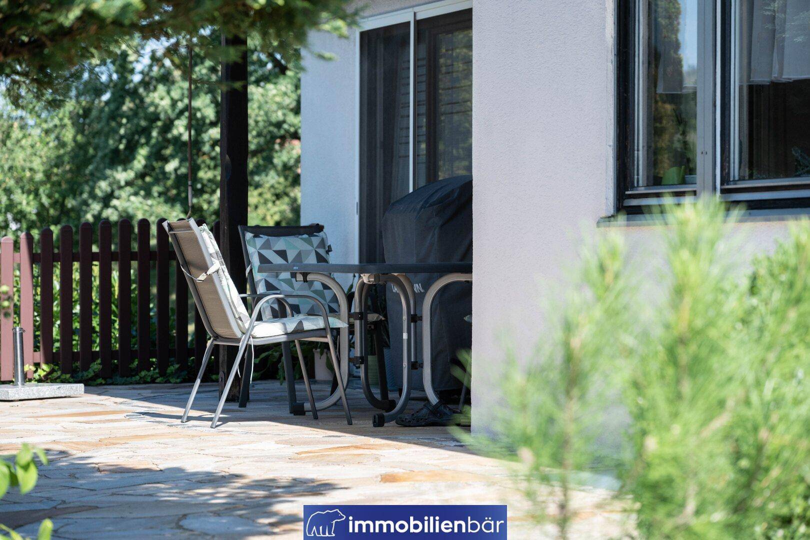 Gemütliche Terrasse mit Gartenmöbeln und Grillbereich, umgeben von einem Holzzaun.