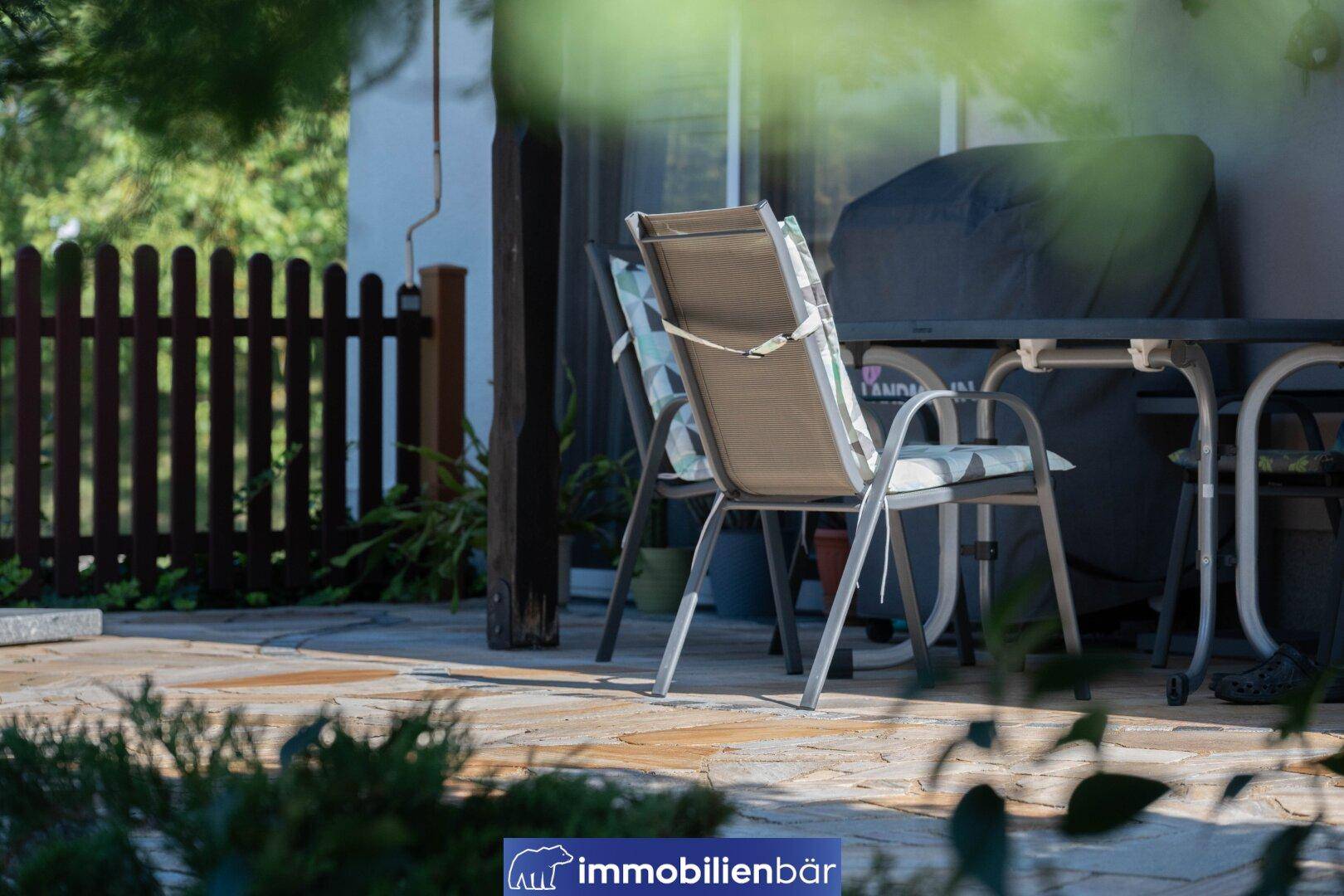 Detailansicht der Terrasse mit Gartenmöbeln und einem Grill, umgeben von Grün.
