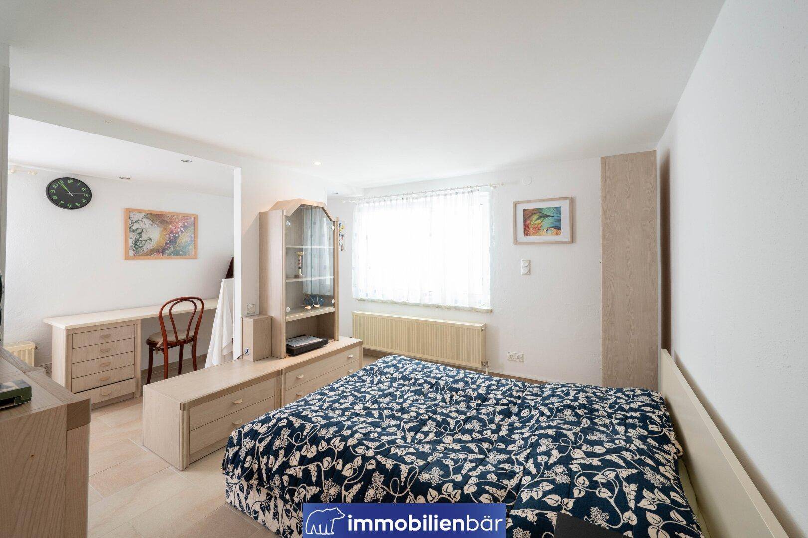 Schlafzimmer mit Doppelbett, Schreibtischbereich und Fliesenboden im Untergeschoss.