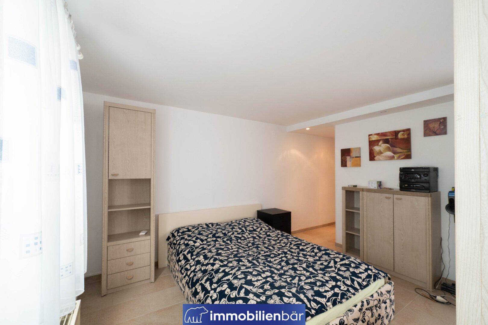 Schlafzimmer mit Einzelbett, Schrank und Fliesenboden im Untergeschoss des Hauses.
