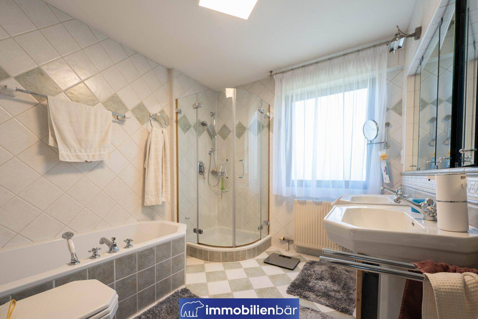 Helles Badezimmer mit Badewanne, Duschkabine, Doppelwaschbecken und Fenster, in gutem Zustand.