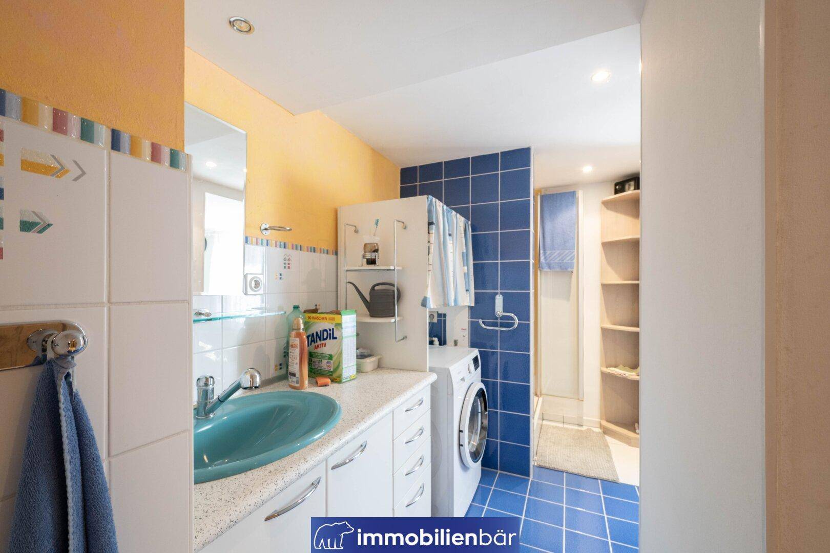 Funktionales Badezimmer mit Waschmaschine, Dusche und farbigen Fliesen, praktisch eingerichtet.