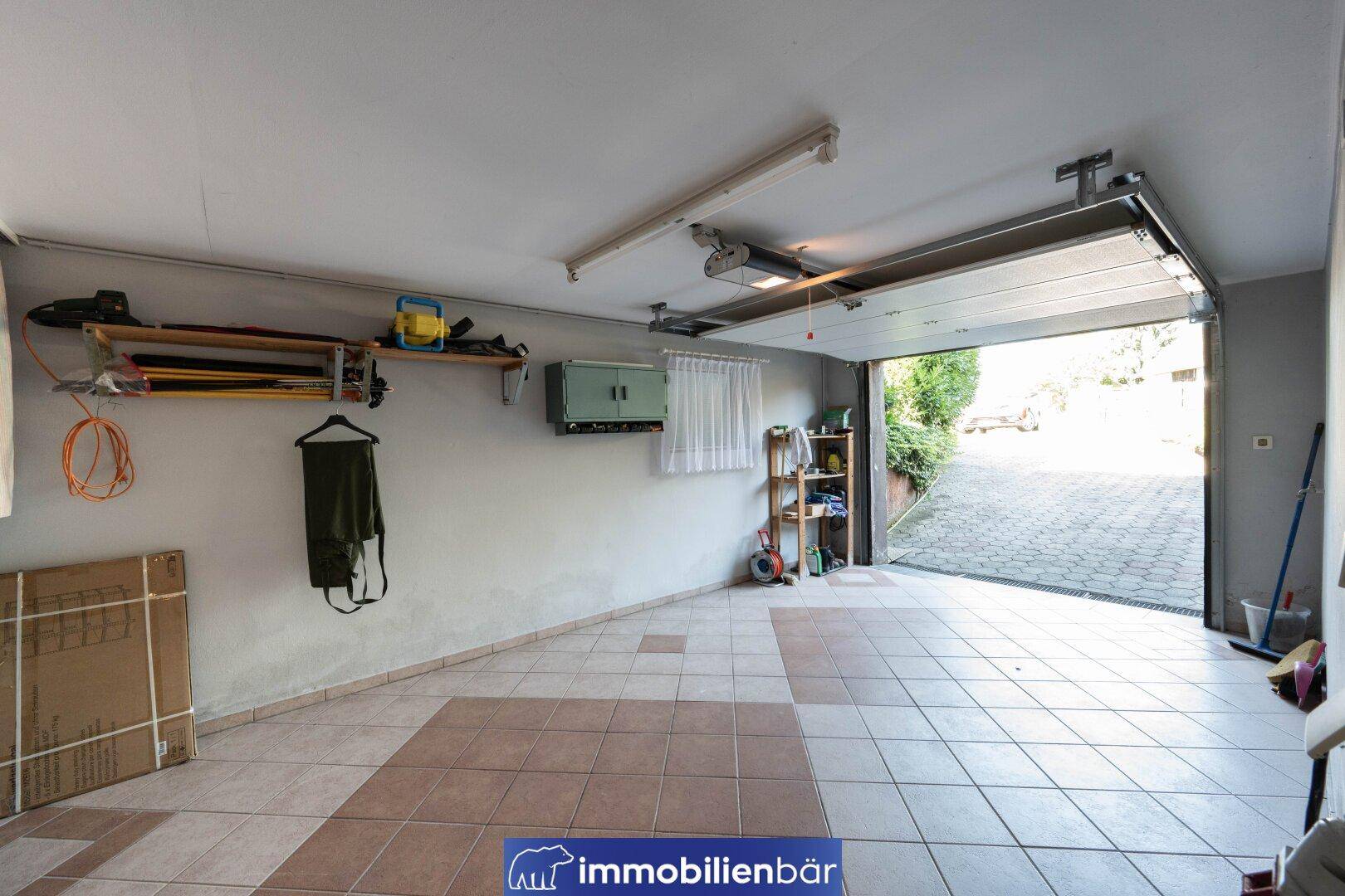 Geräumige Garage mit Fliesenboden und offenem Garagentor, bietet viel Stauraum.
