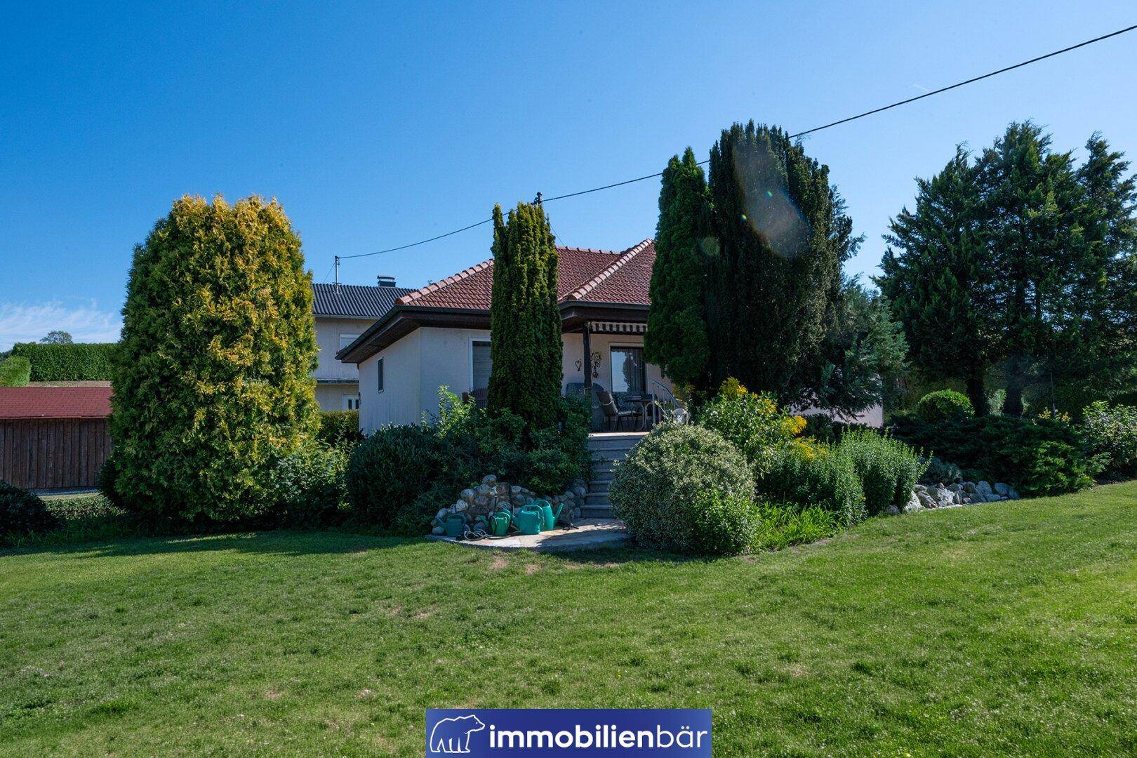 Weitläufiger Gartenbereich mit üppiger Bepflanzung und dem Haus im Hintergrund an einem sonnigen Tag.