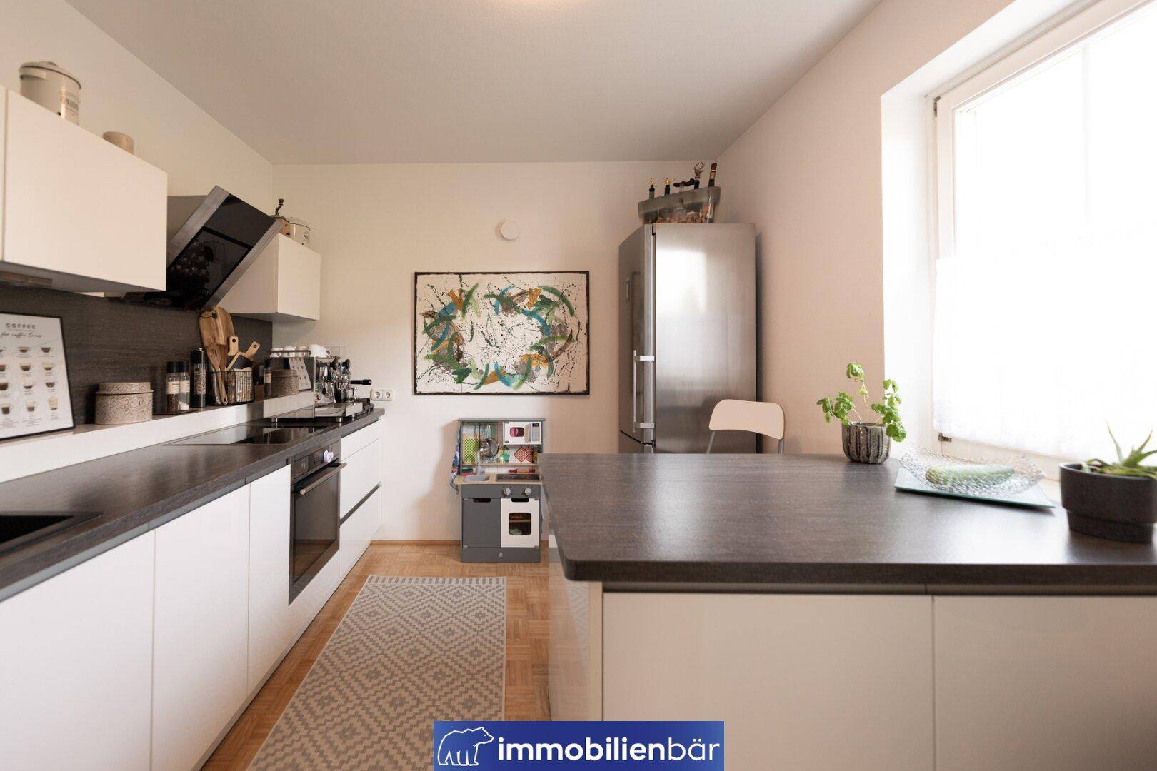 Moderne Küche mit weißen Schränken, dunklen Arbeitsplatten und integriertem Backofen.