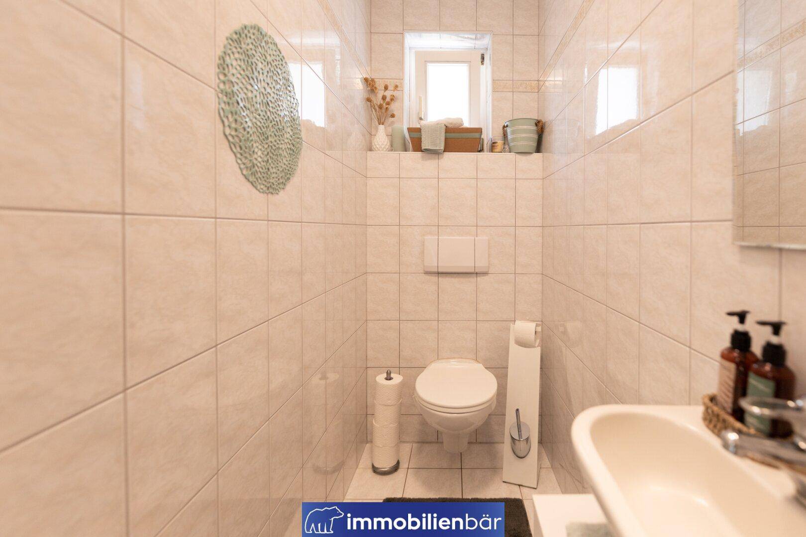 Gäste-WC mit wandhängendem WC, kleinem Waschbecken und Fenster für Tageslicht.