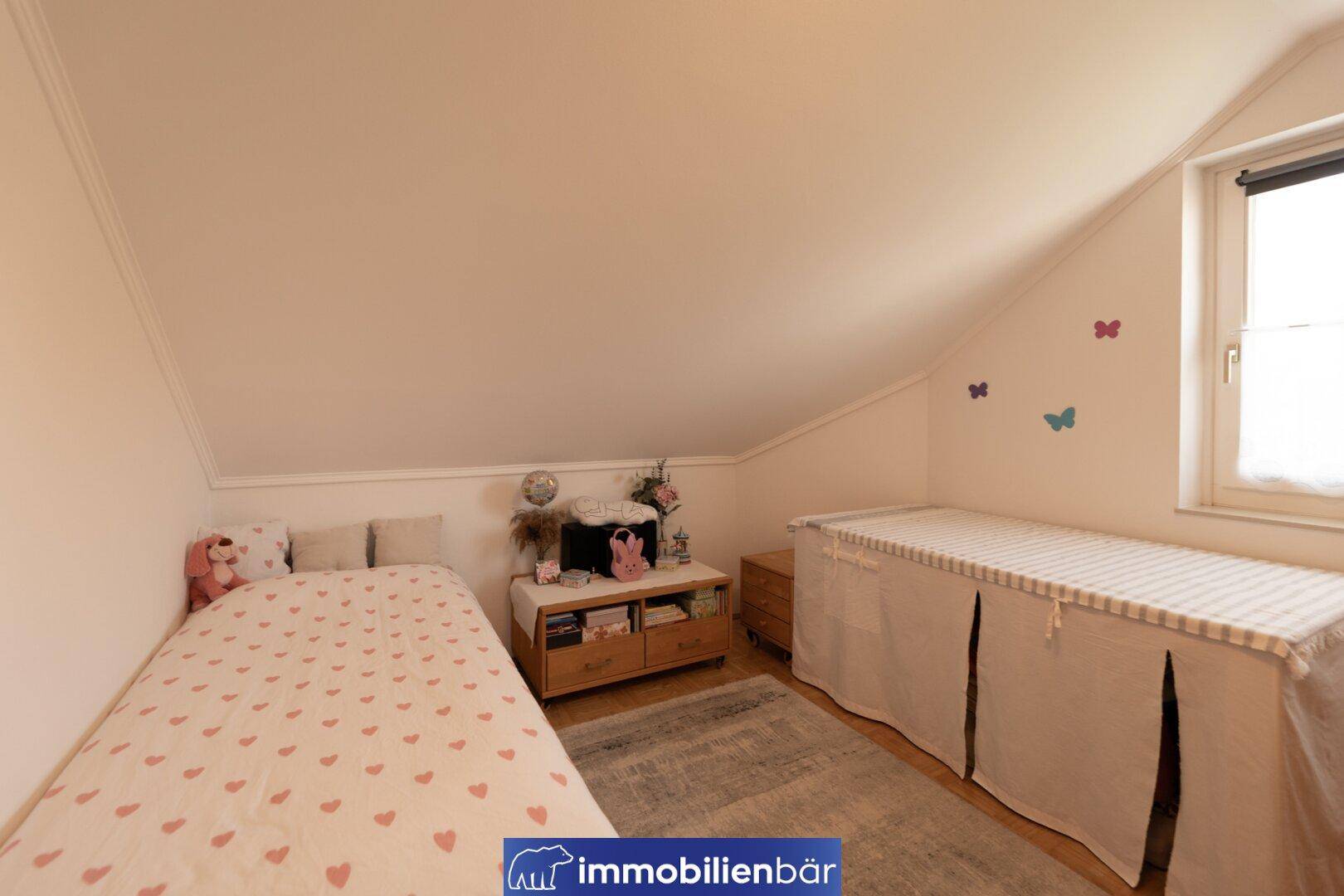Gemütliches Schlafzimmer im Dachgeschoss mit schräger Decke und Fenster.