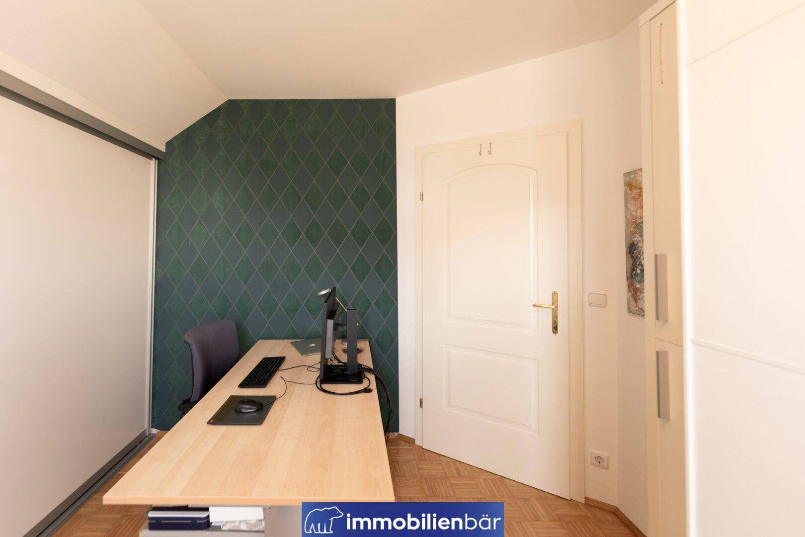 Arbeitszimmer mit Schreibtisch, Schrank und einer Akzentwand in dunklem Grün.