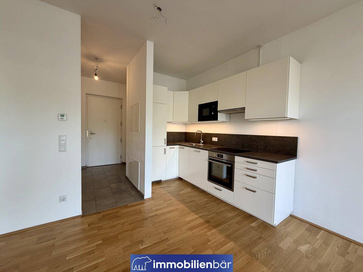 Moderne Einbauküche in Weiß mit dunkler Arbeitsplatte und Holzfußboden in einem offenen Wohnbereich.