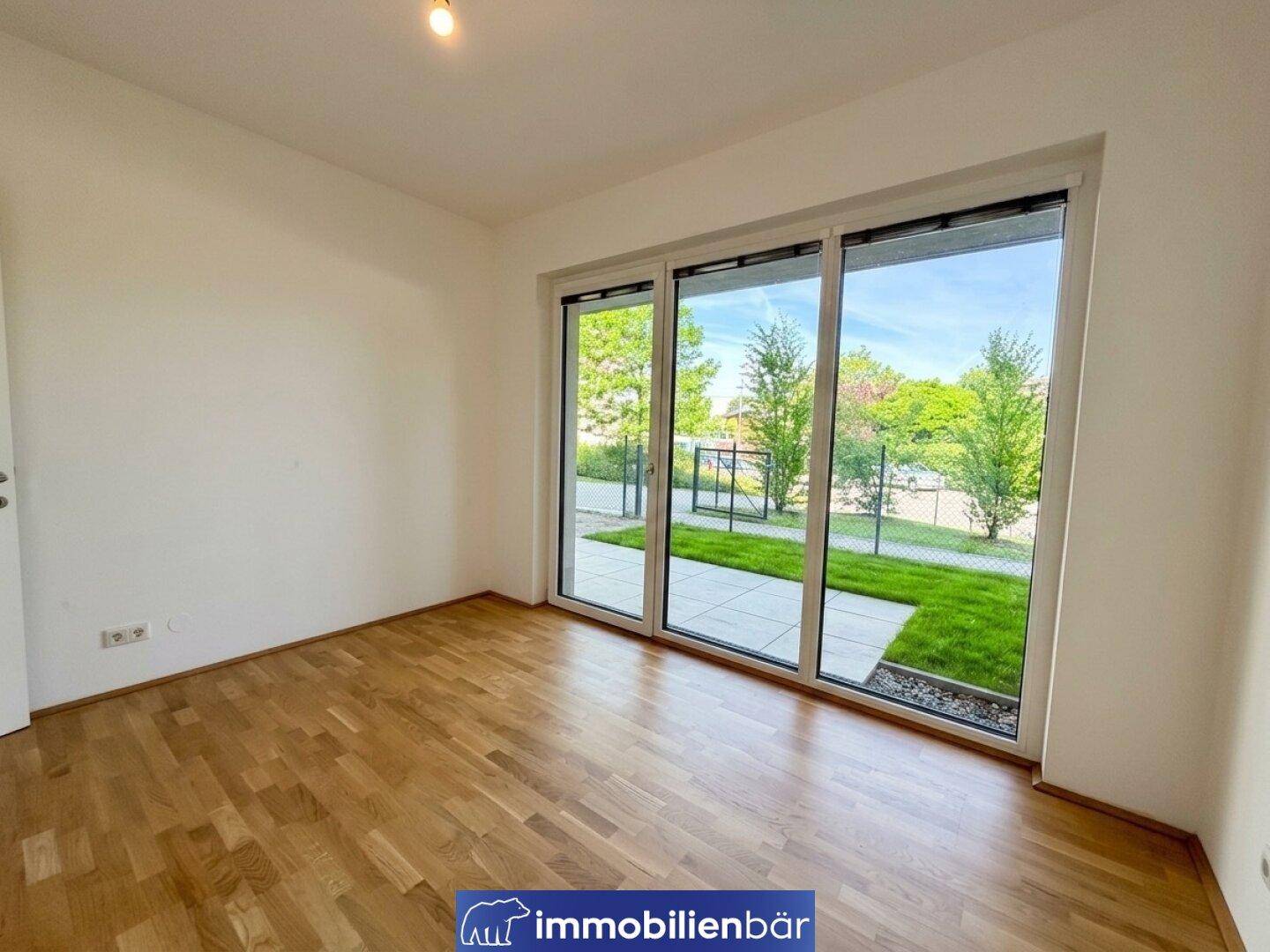 Heller Raum mit Holzfußboden und großer Schiebetür zum Gartenbereich.