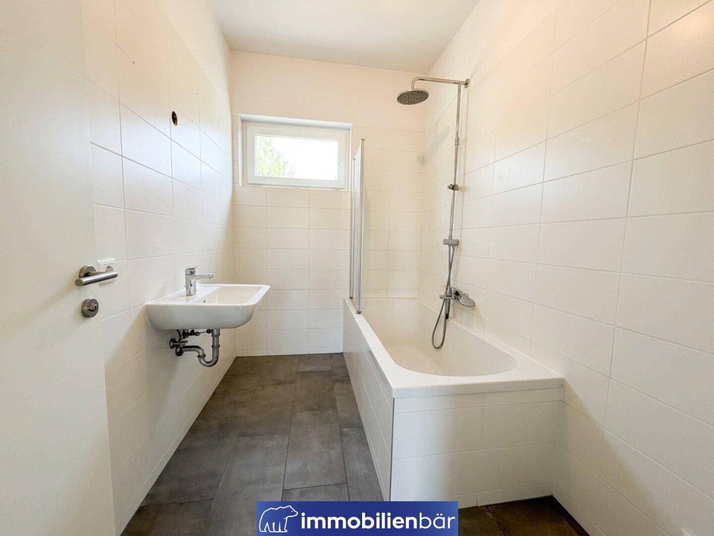 Helles Badezimmer mit Badewanne, Duschfunktion, Waschbecken und Fenster.