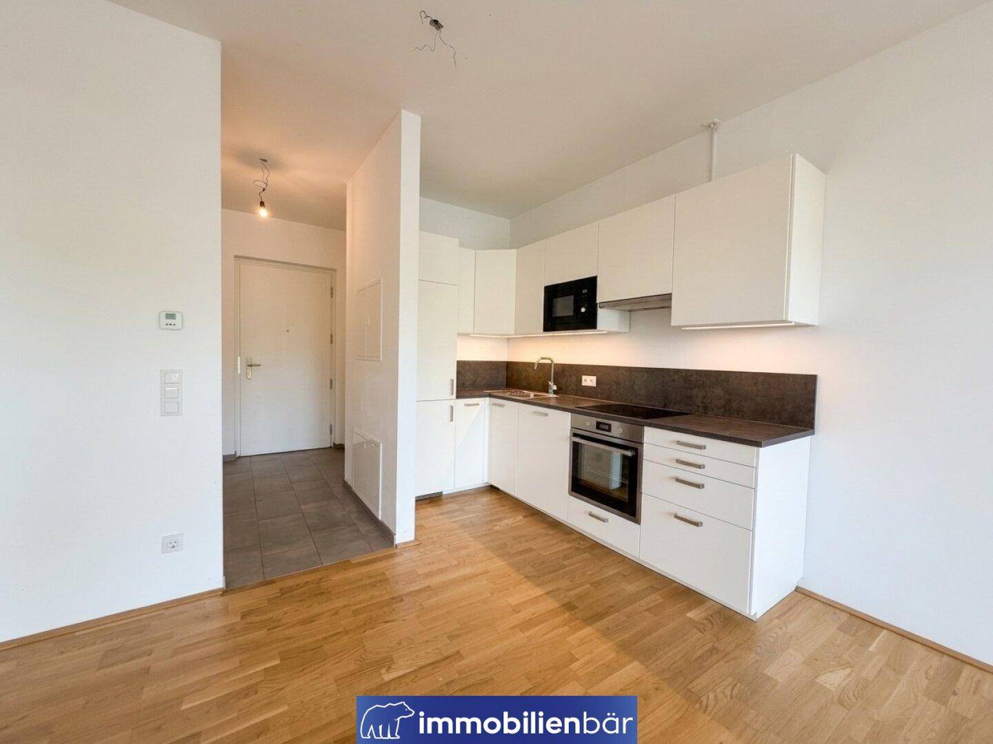 Moderne Einbauküche in Weiß mit dunkler Arbeitsplatte und Holzfußboden in einem offenen Wohnbereich.