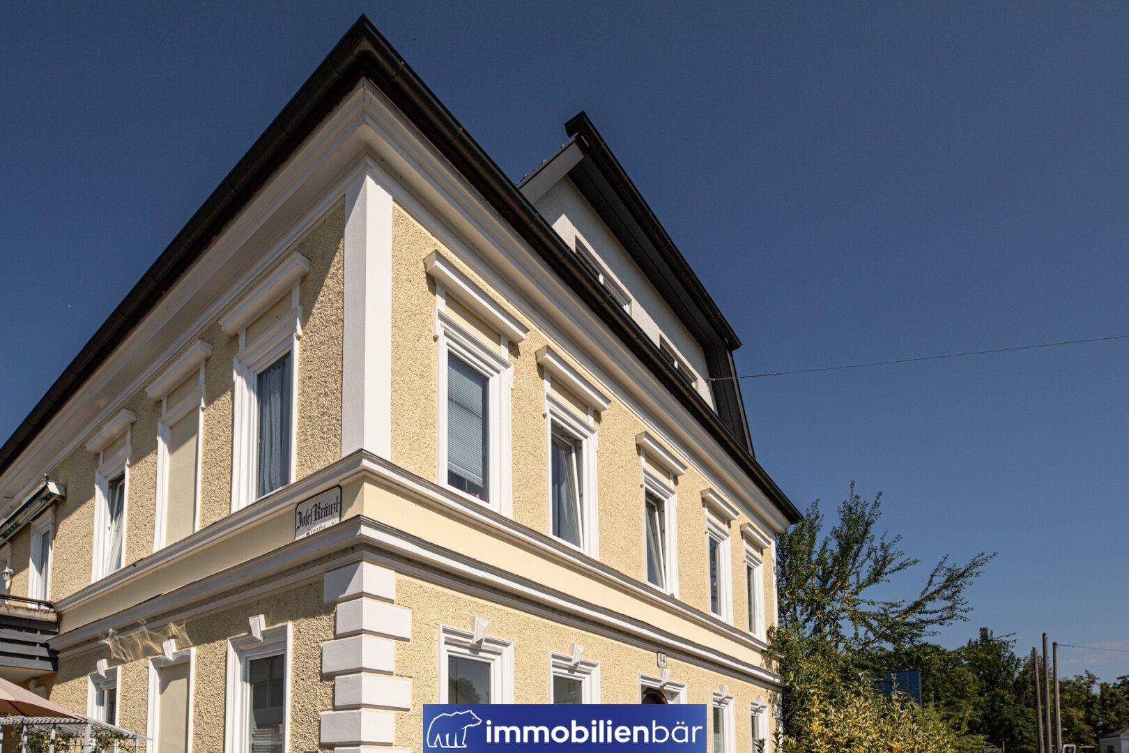 Detailansicht der gelben Fassade mit weißen Fensterrahmen und dekorativen Elementen an der Gebäudeecke.